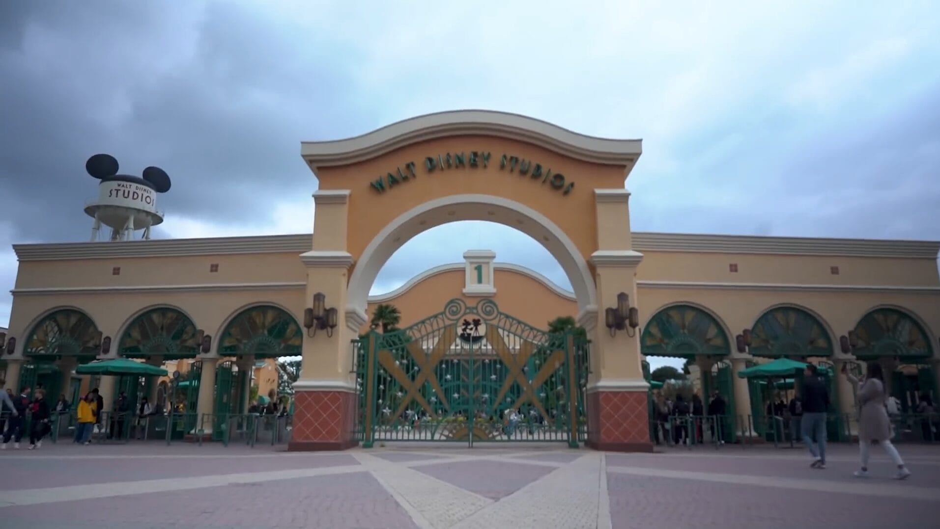 The entrance gate of Walt Disney Studios with a large archway, welcoming Disney Park fans as people gather for a video.