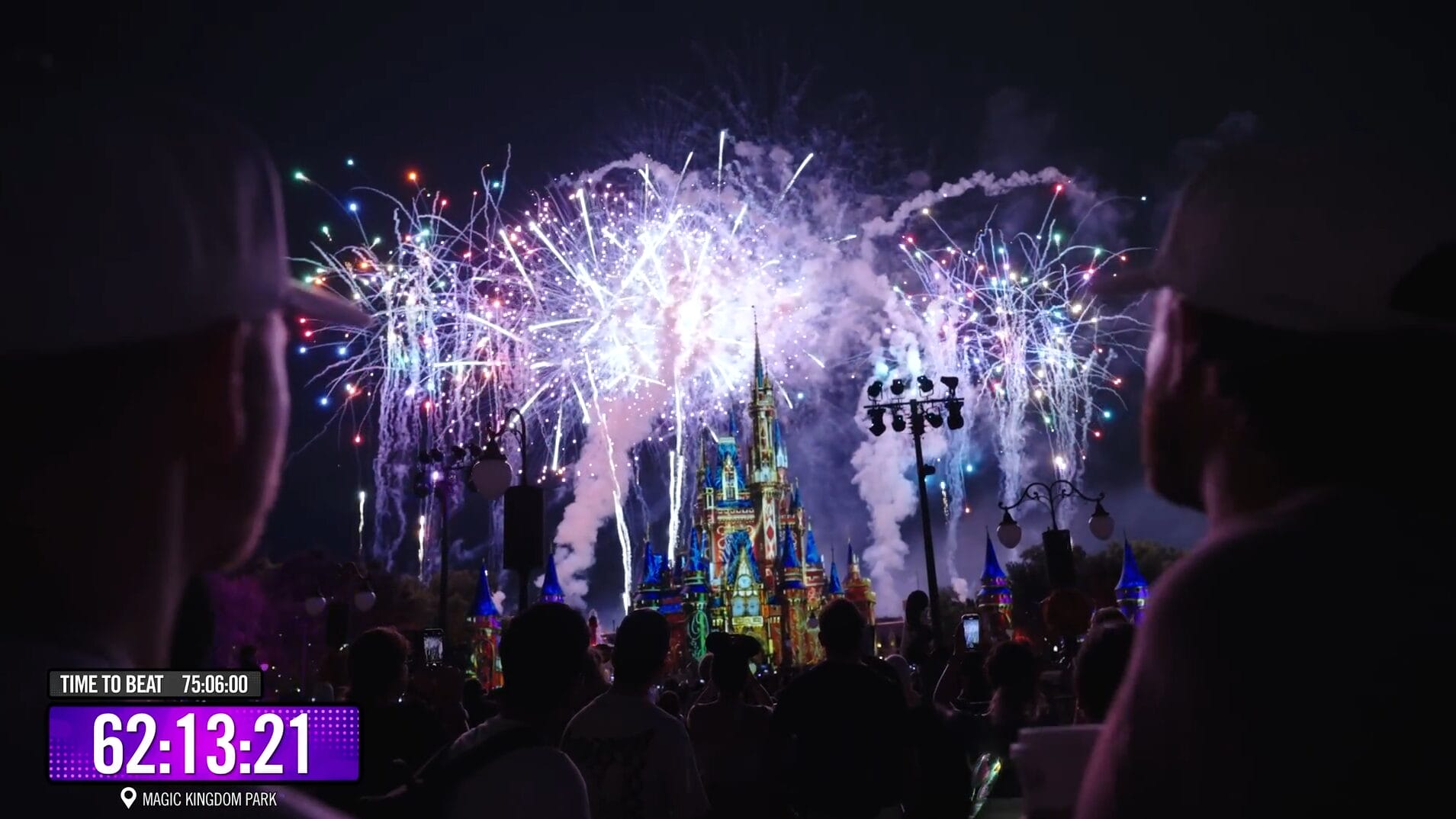 Colorful fireworks explode above a lit Disney Park castle at night, with a crowd watching and a timer in the lower left.