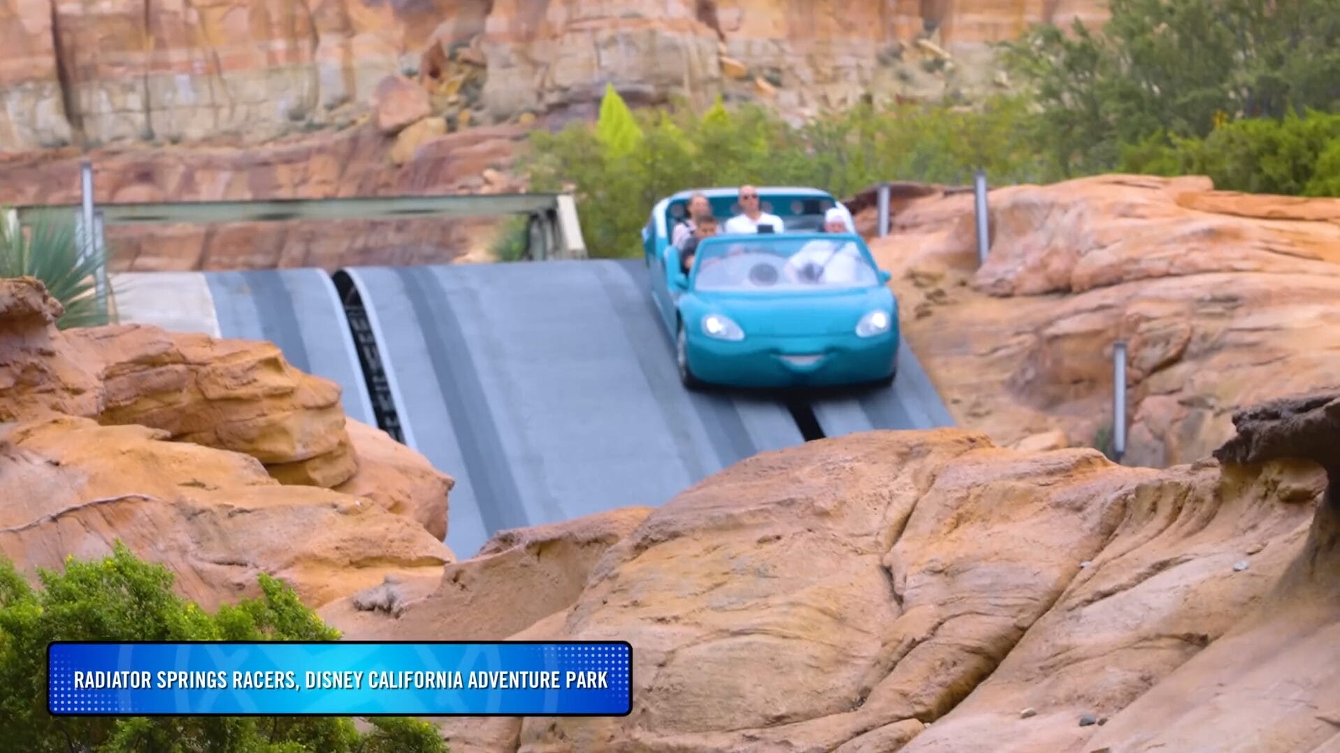 A blue car-shaped ride vehicle with passengers descends a hill at Disney Park’s Radiator Springs Racers.