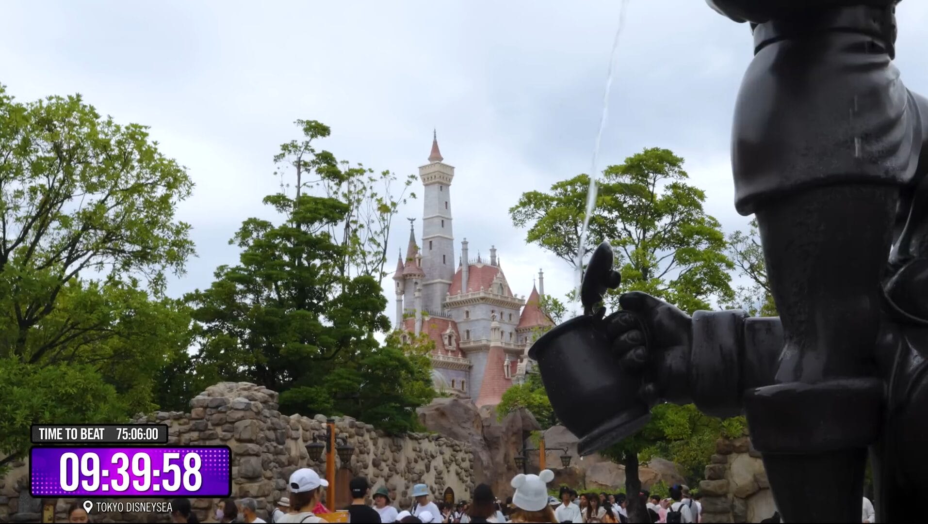 A castle rises behind trees as a statue pours water; people stroll under cloudy skies at a Disney Park.