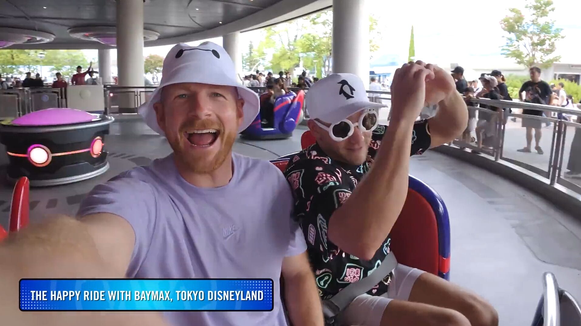 Two excited men in hats and sunglasses pose for a VIDEO selfie on a ride at the Disney Park, smiling brightly.