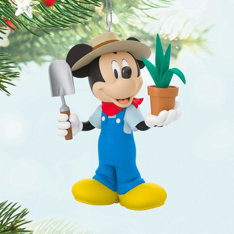 Mickey Mouse ornament in overalls, with plant and trowel, stands before a Christmas tree reminiscent of Main Street, U.S.A. décor.