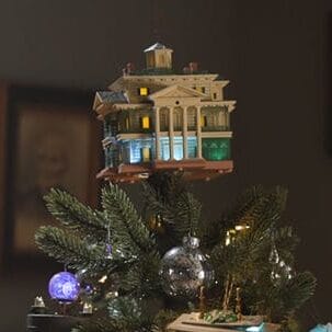 A Christmas tree decorated with Disney Parks Keepsake Ornaments, glowing blue ghosts, and a Haunted Mansion model topper.