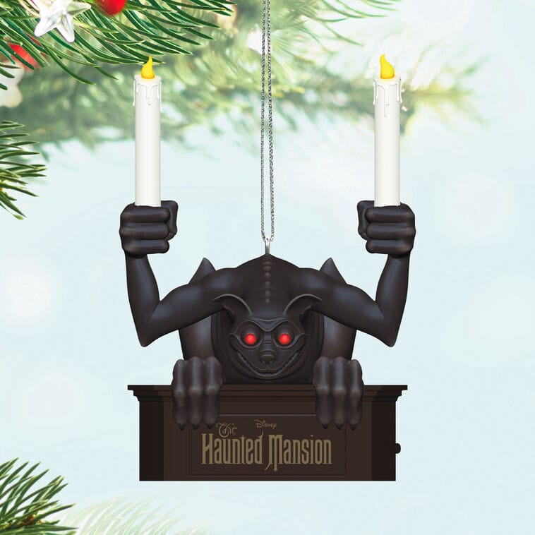 Black gargoyle ornament with red eyes holds two candles, hanging on a branch—Disney Parks style, evoking Fantasyland details.