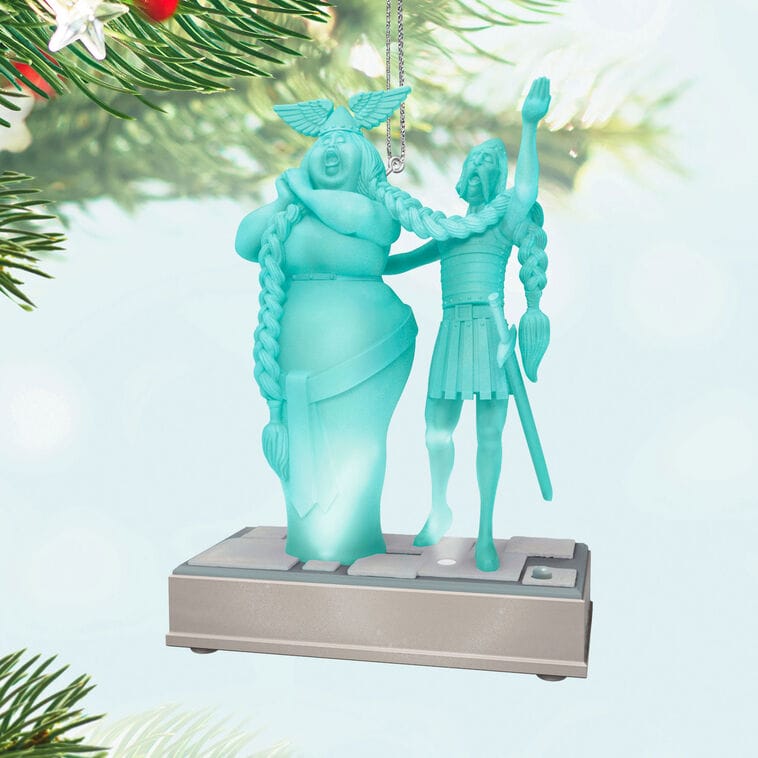 Teal Hallmark ornament with two braided figures in classical attire hangs on a Christmas tree, like decor found at Disney parks.