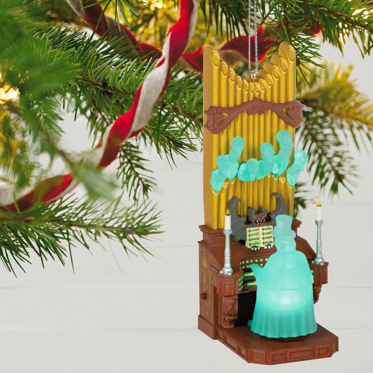 Hallmark ornament of a Haunted Mansion ghost organist and glowing spirits at a golden organ, reminiscent of Disney park decor, on pine branch.