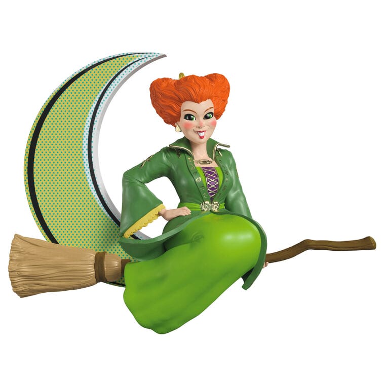 A smiling woman in a green dress sits on a broomstick before a crescent moon, evoking Disney Parks magic—perfect for ornament fans.