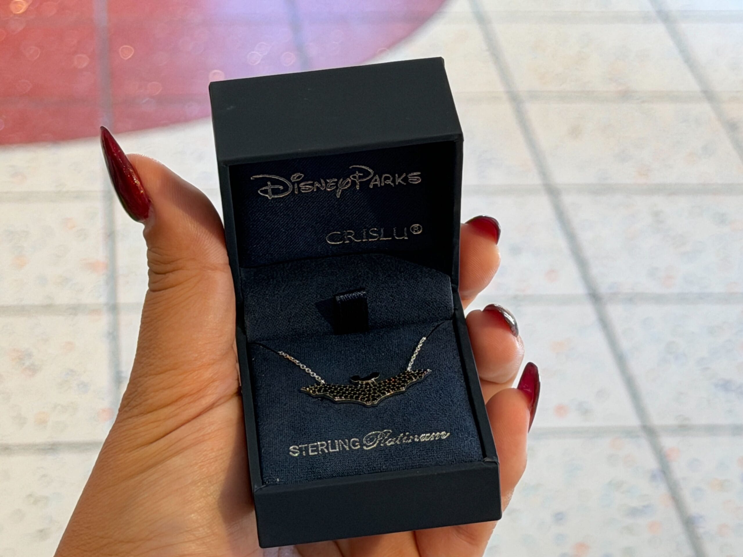 A hand displays a CRISLU necklace in its box at the Walt Disney World Halloween Trunk Show, near Cinderella Castle.