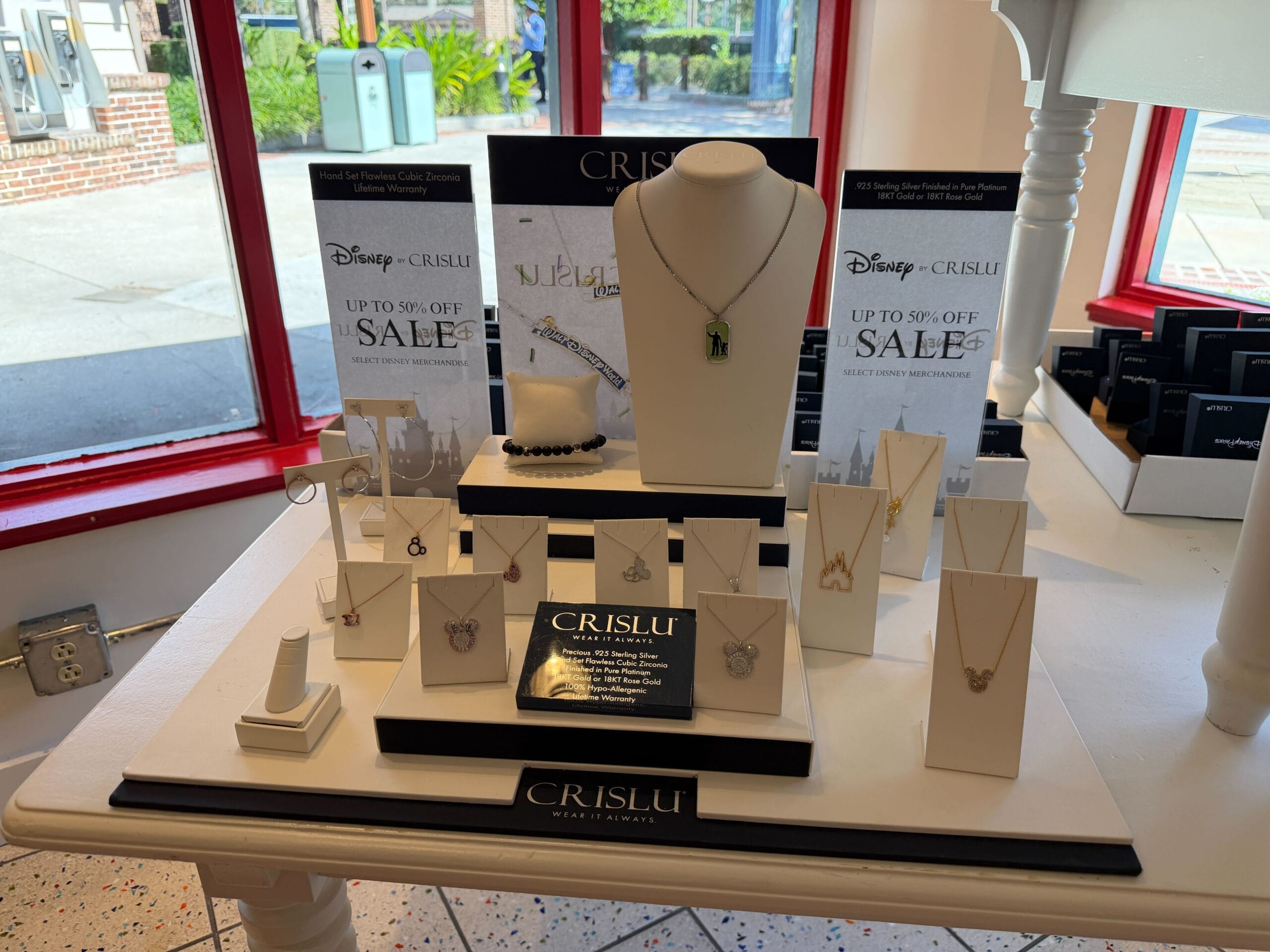 CRISLU Disney jewelry on display in a park shop, with Halloween Trunk Show sale signs, capturing Disney magic in each piece.