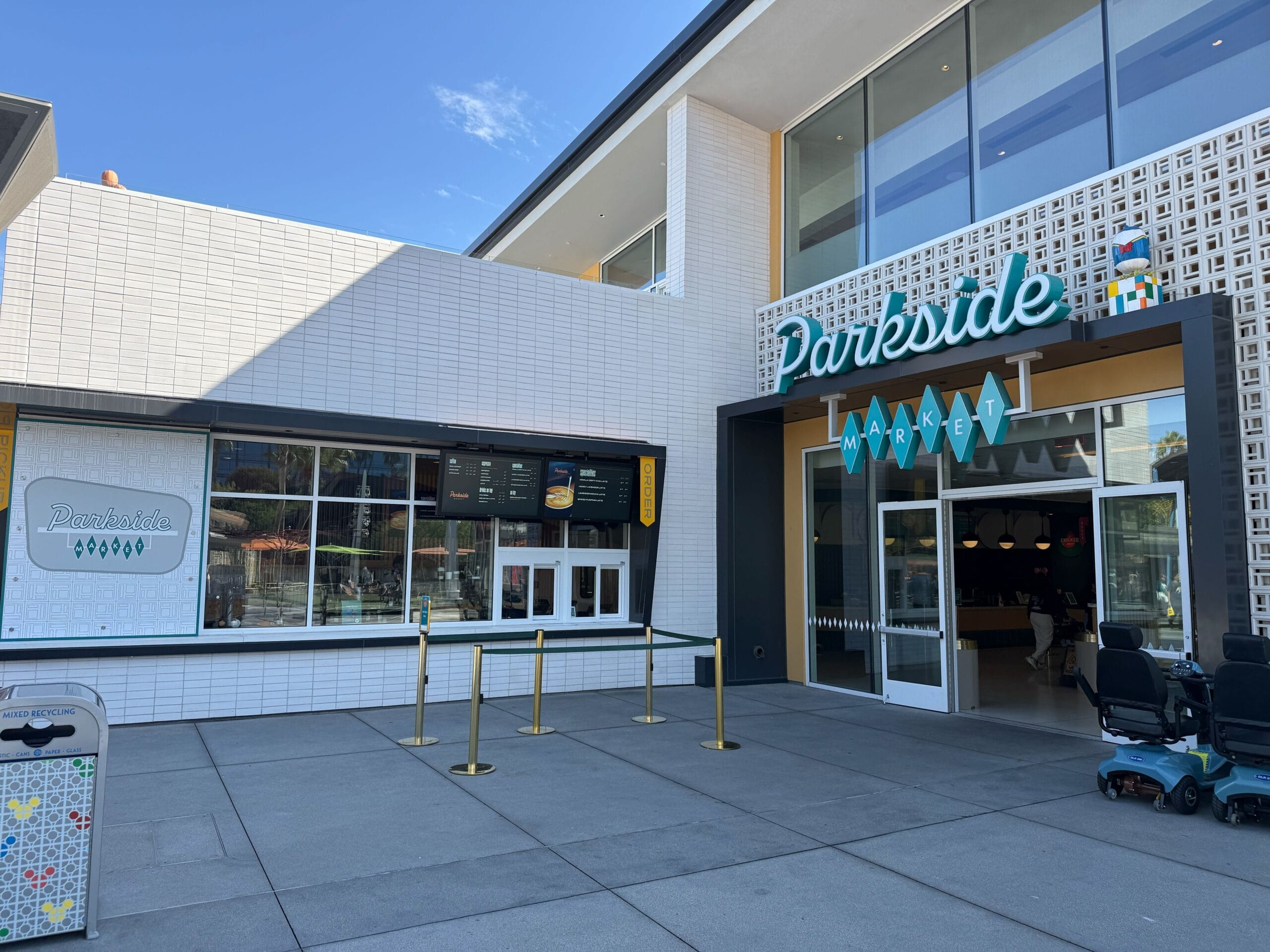 Parkside Market entrance with takeout window, menu, and outdoor queue ropes—reminiscent of Disney park food stands on a sunny day.
