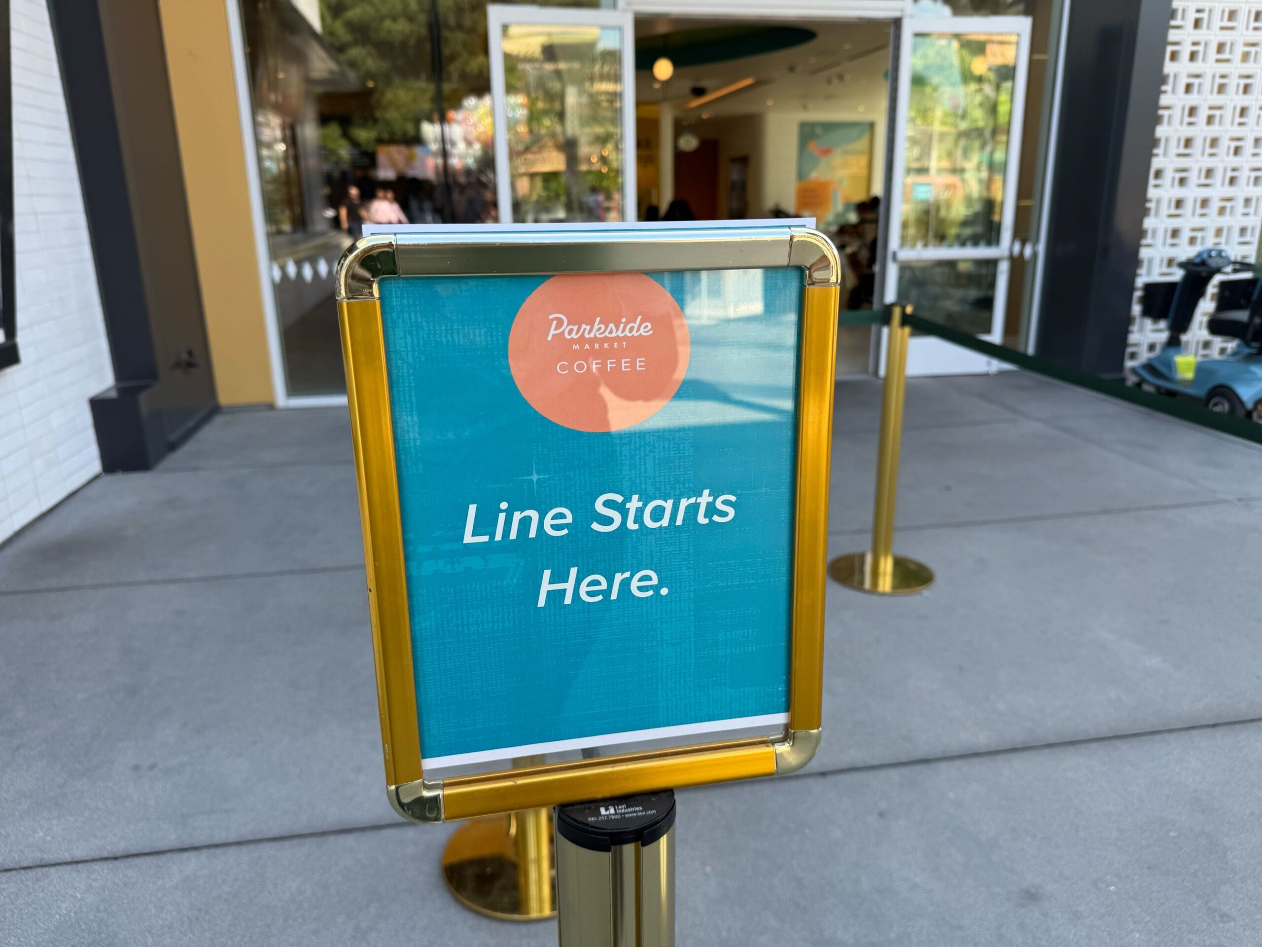 A sign that says "Parkside Coffee Line Starts Here" stands outside a coffee shop, similar to directional signs in Disney Parks.