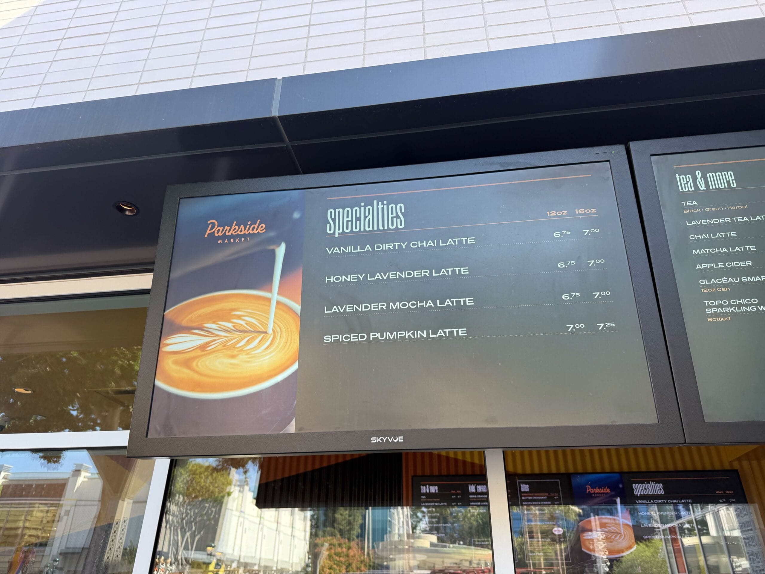 Digital menu board at Parkside Market in Disney park, listing specialty lattes like vanilla chai, honey lavender, and spiced pumpkin.