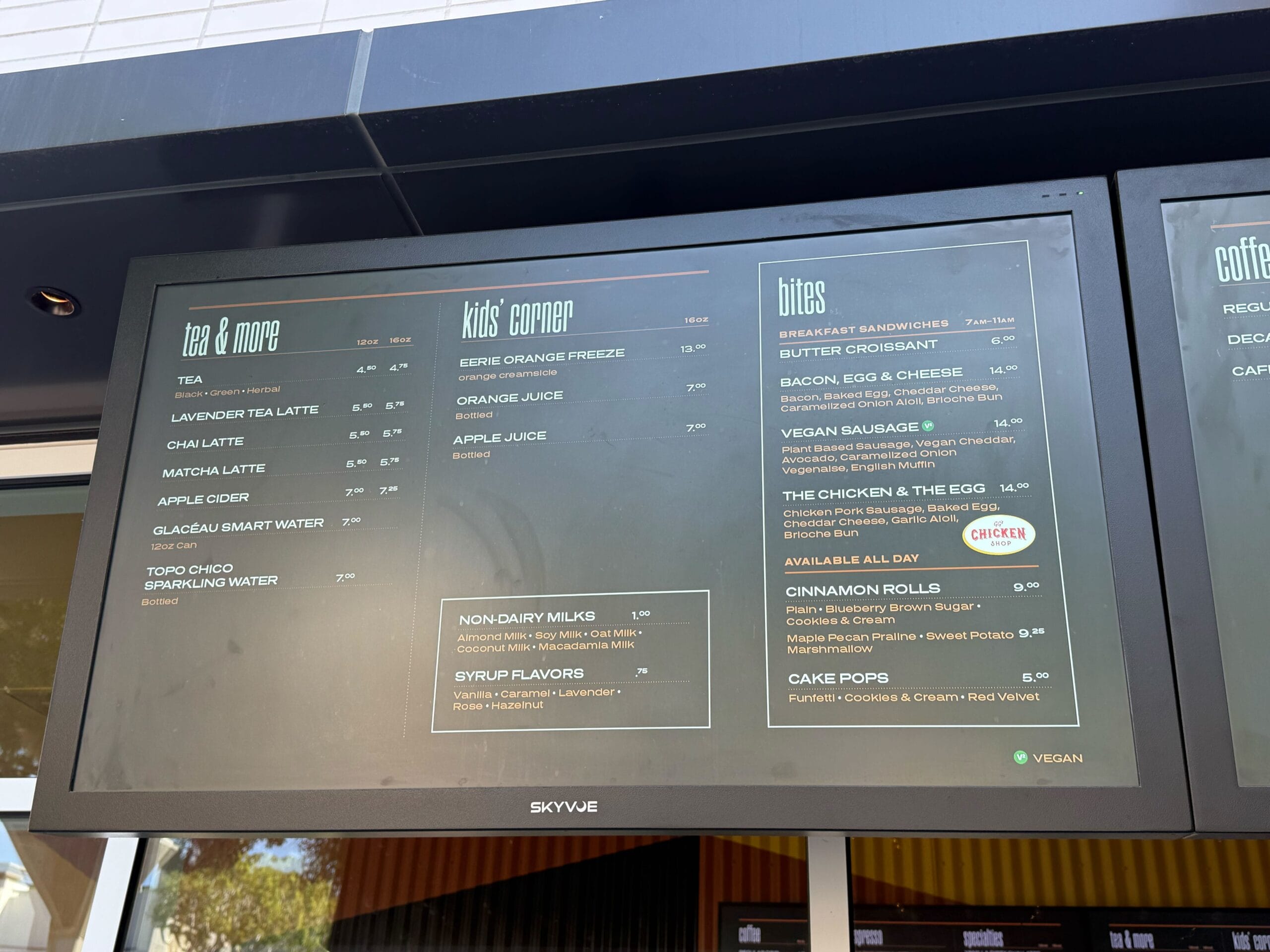 Menu board at a Disney park cafe lists drinks, kids' meals, and snacks, highlighting vegan and non-dairy choices for guests.