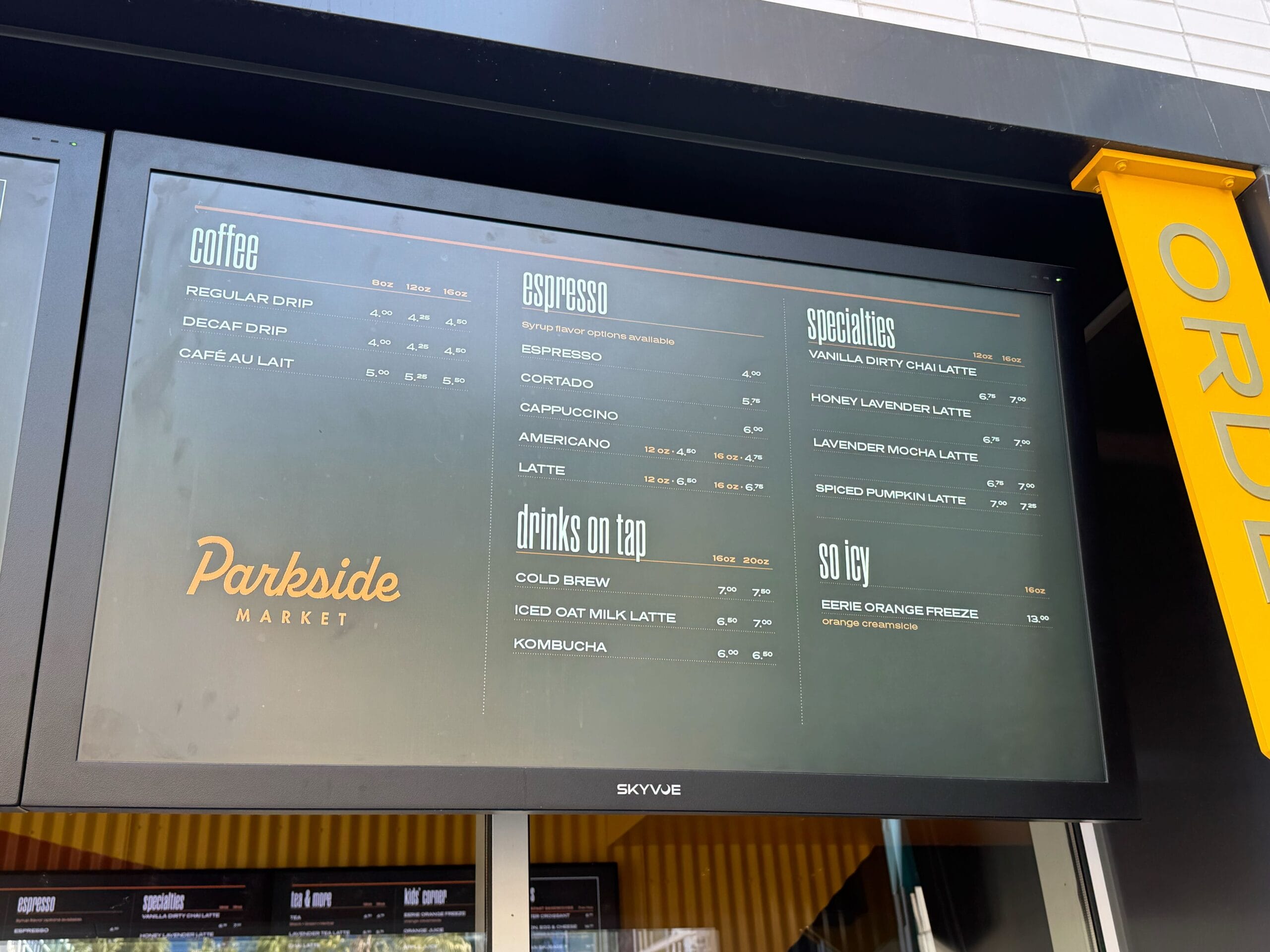 Digital menu board at Parkside Market in a Disney park, listing coffee and specialty drinks—no castle like Cinderella or Sleeping Beauty.