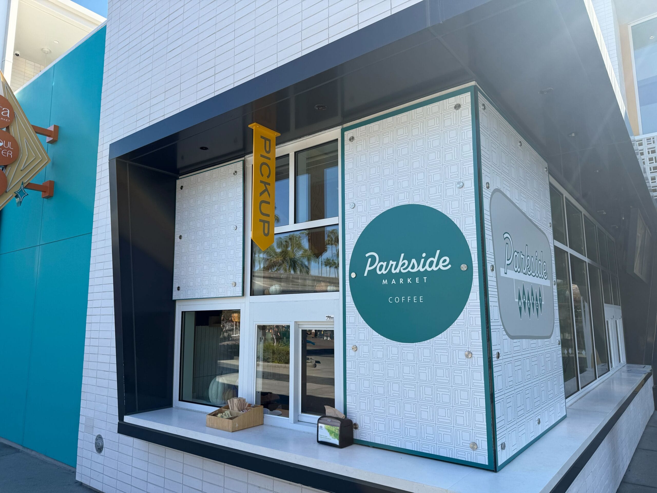 Parkside Market Coffee pick-up window with basket on ledge and green sign on clean white tiles, not themed like any Disney castle.