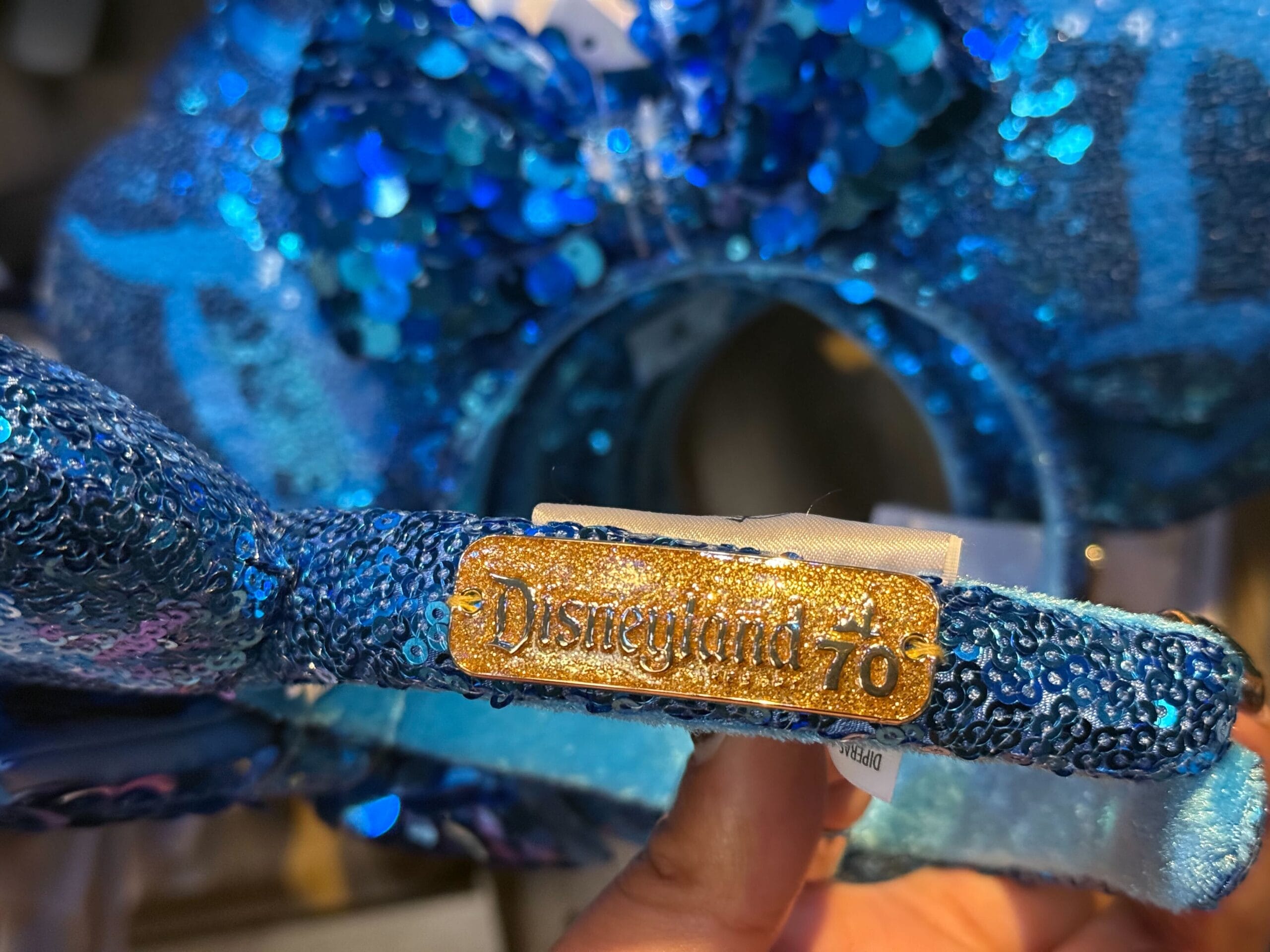 Close-up of a blue sequined Disneyland 70th headband held by a hand, echoing park-exclusive merchandise from Disney resorts.