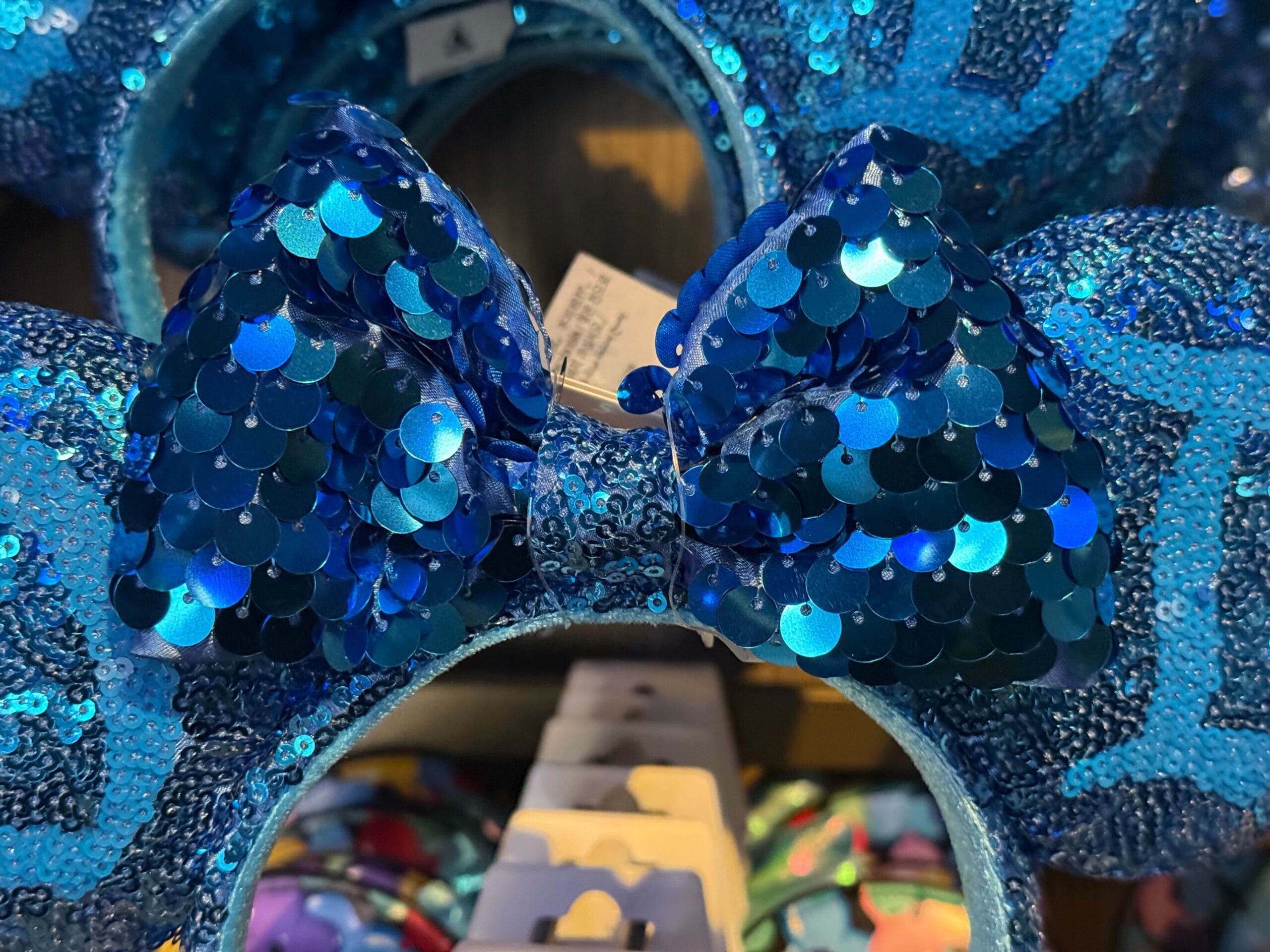 Close-up of a blue sequined bow with large round sequins on a matching headband, similar to Minnie ears at Disney parks.