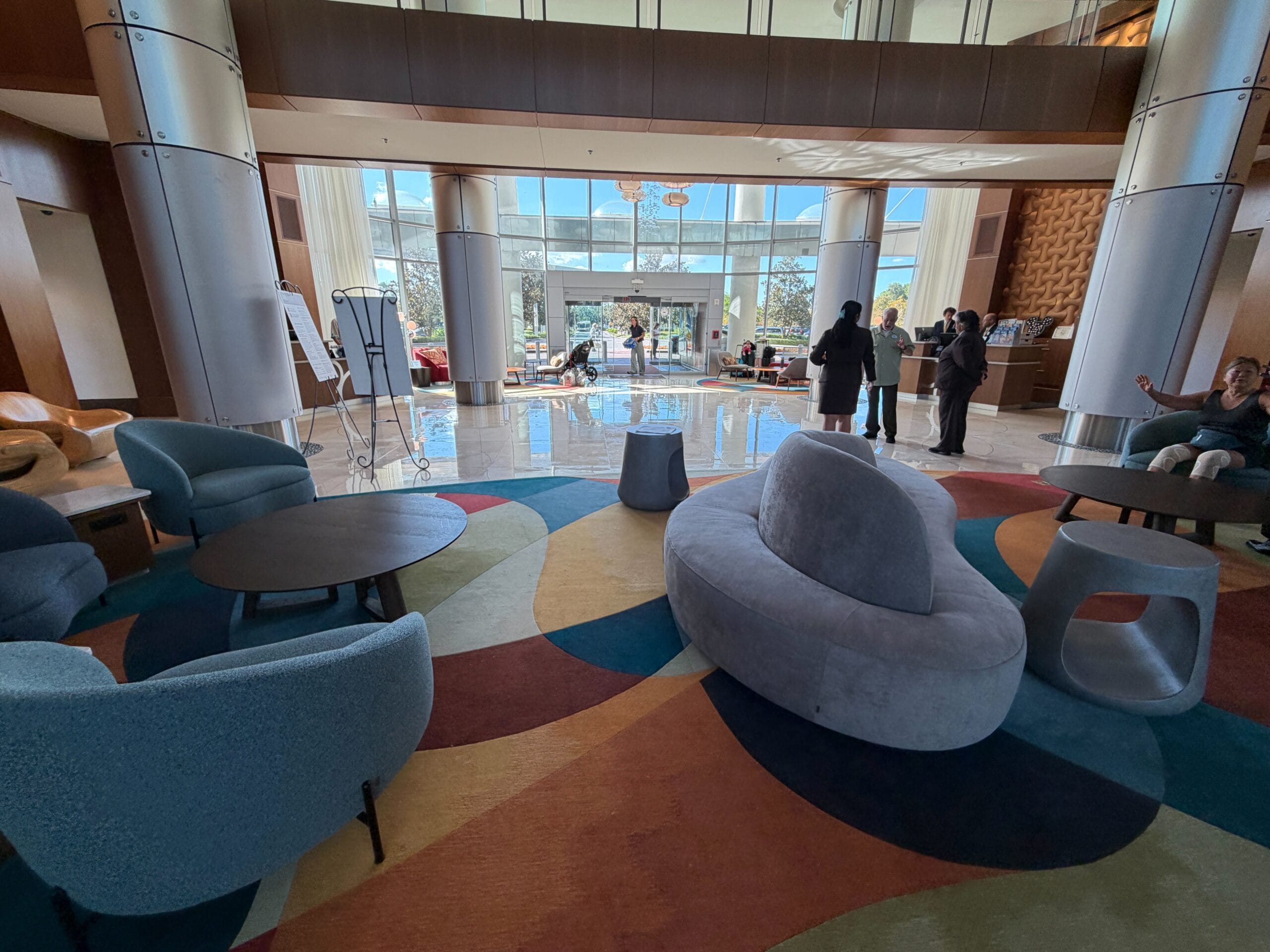 Contemporary Bay Lake Tower hotel lobby at Disney, featuring a vibrant rug, sleek curved seats, big windows, and bustling guests.