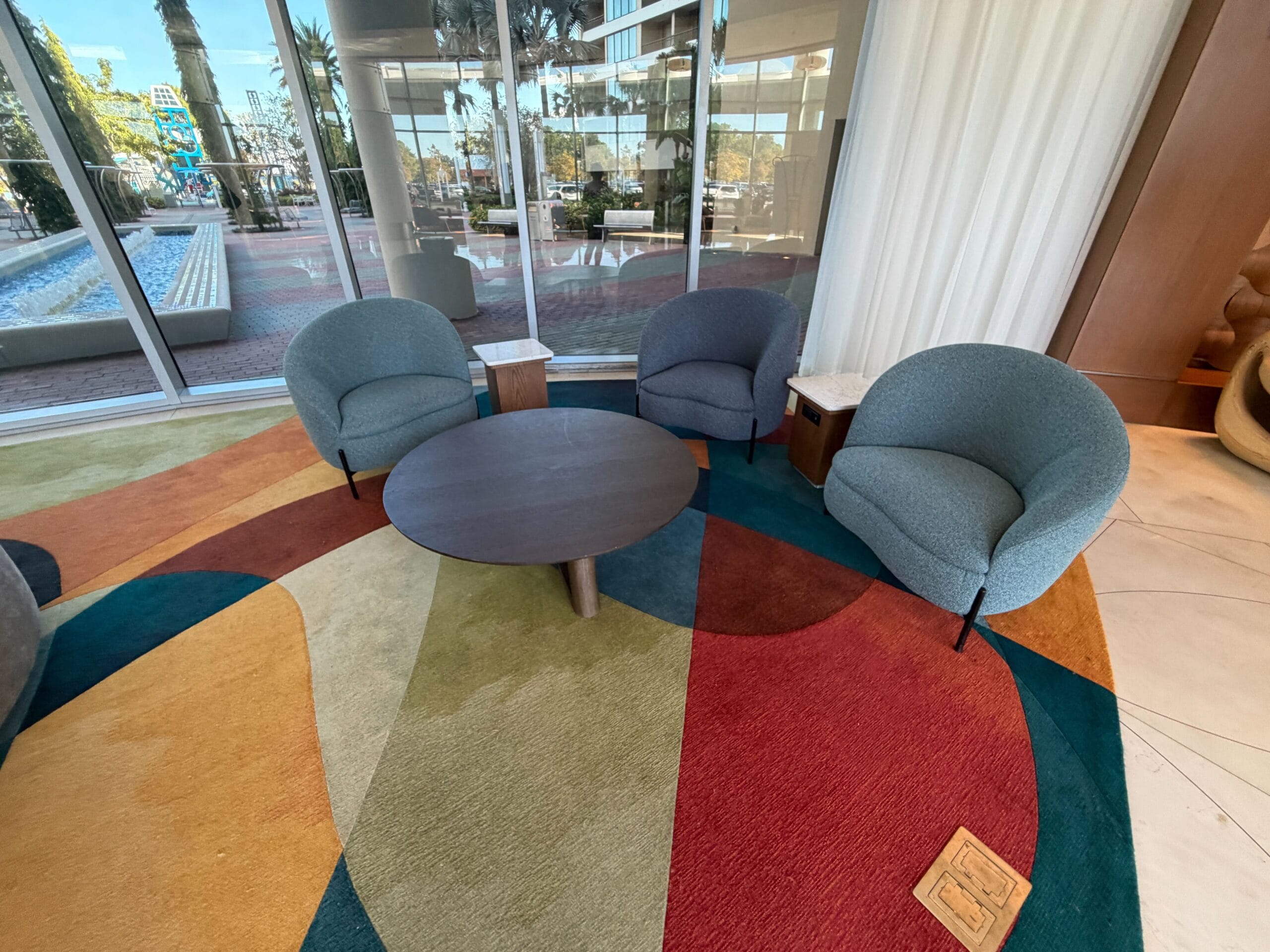 Three curved armchairs and a round table on a geometric rug in Disney’s Contemporary Resort lounge, near large glass windows.