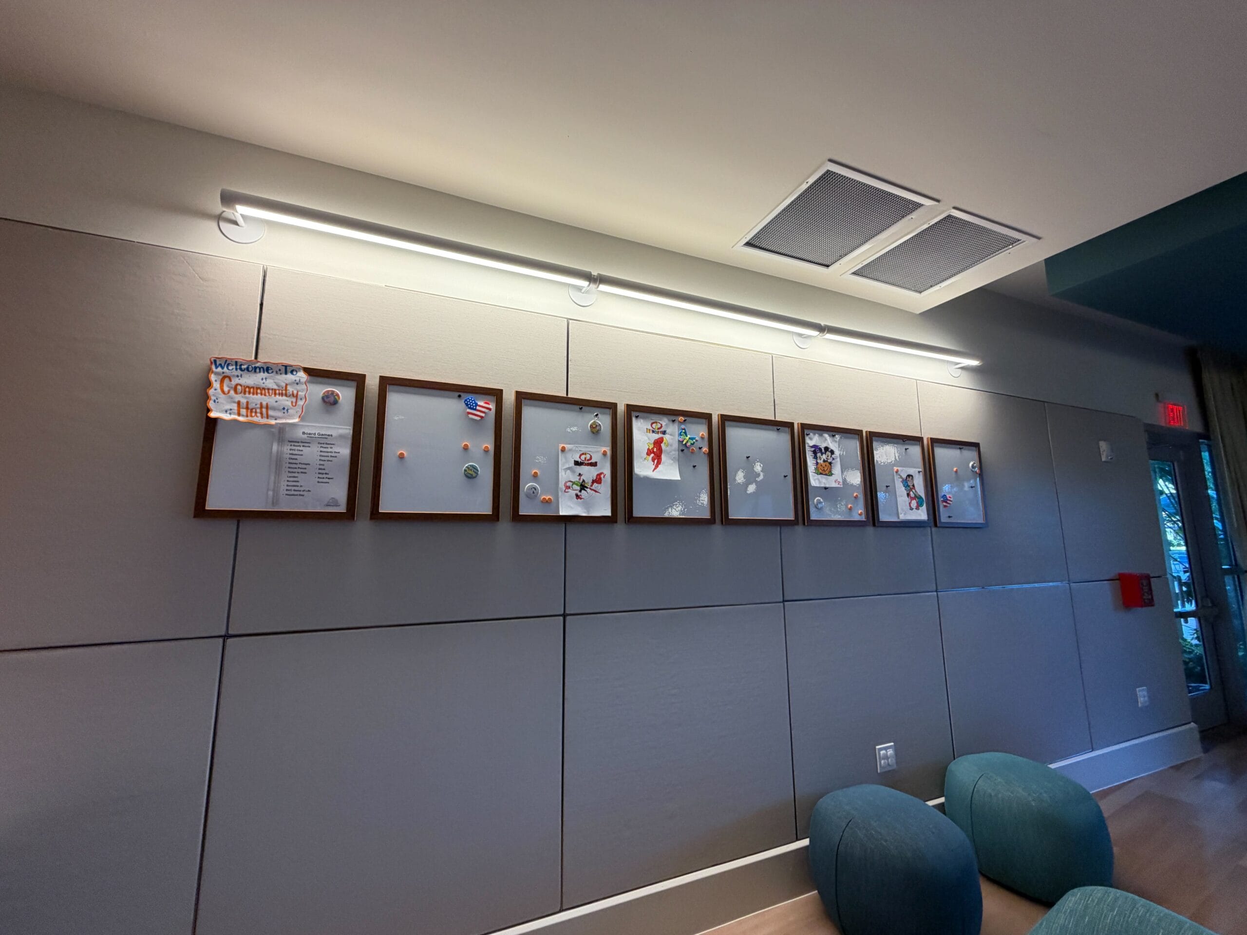 A line of bulletin boards on a gray wall in a renovated Bay Lake Tower room, featuring sleek blue chairs. No castle views here.