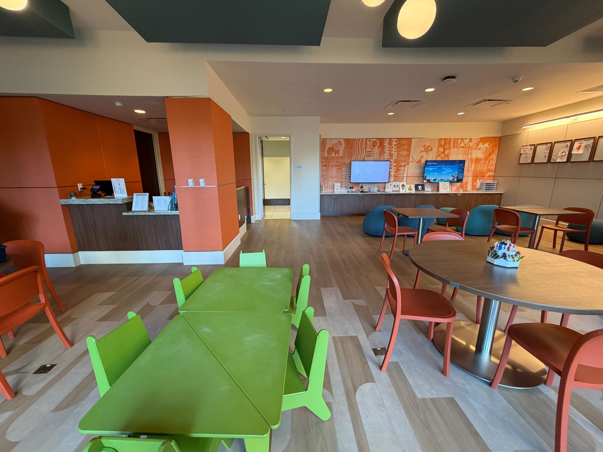 Bright playroom with green kids’ table, orange chairs, and TV—evoking Disney’s Contemporary Resort’s signature vibrant decor style.