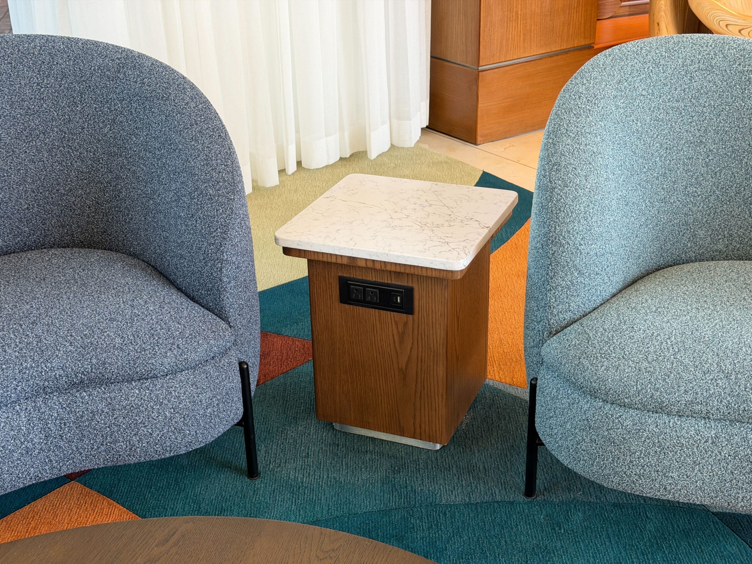 A wooden side table with power outlets sits between blue armchairs, echoing Bay Lake Tower at Disney World’s sleek, modern design.
