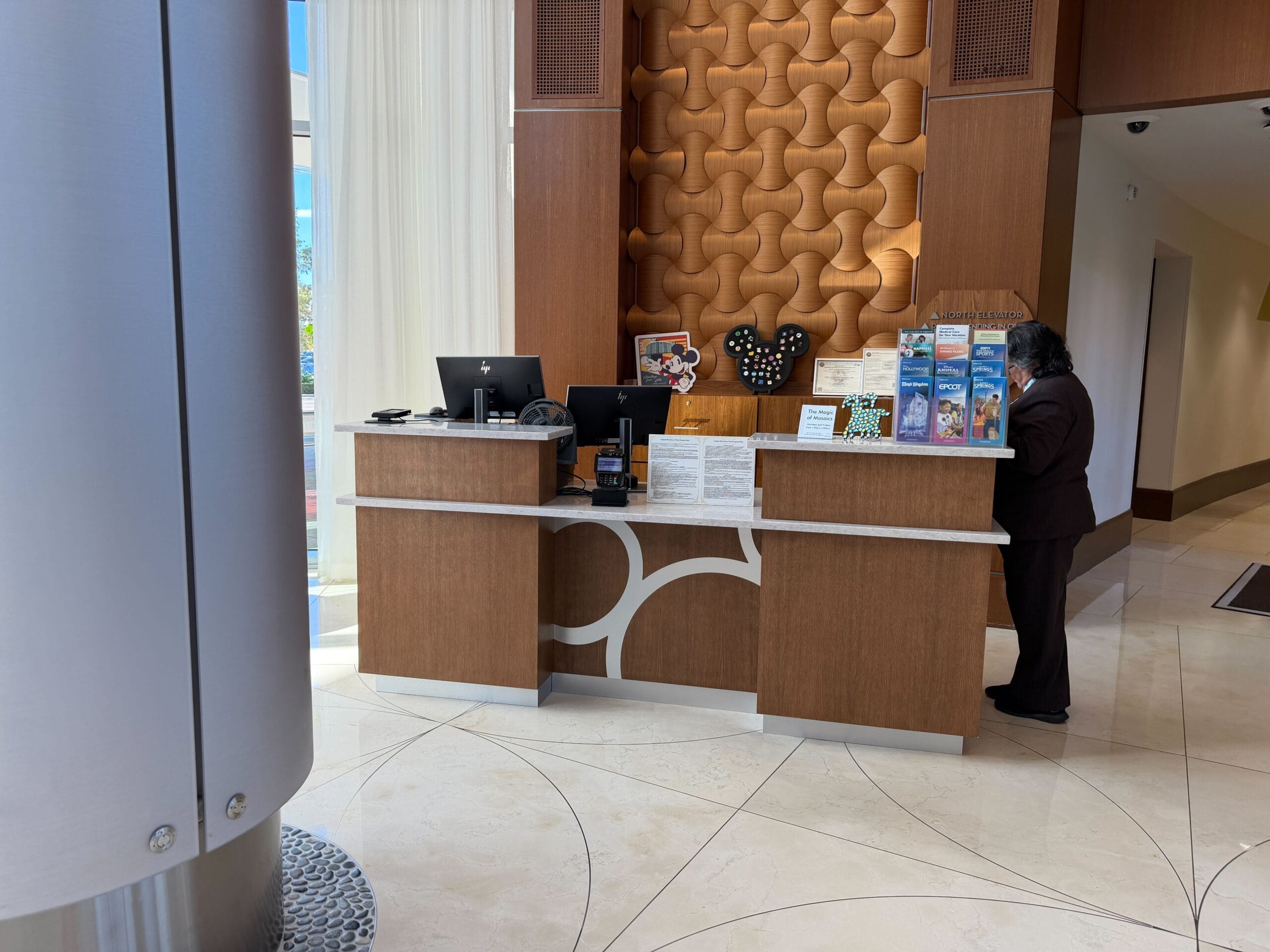 A guest stands at Disney’s Contemporary Resort concierge desk, brochures and computers on the counter, no castle visible here.