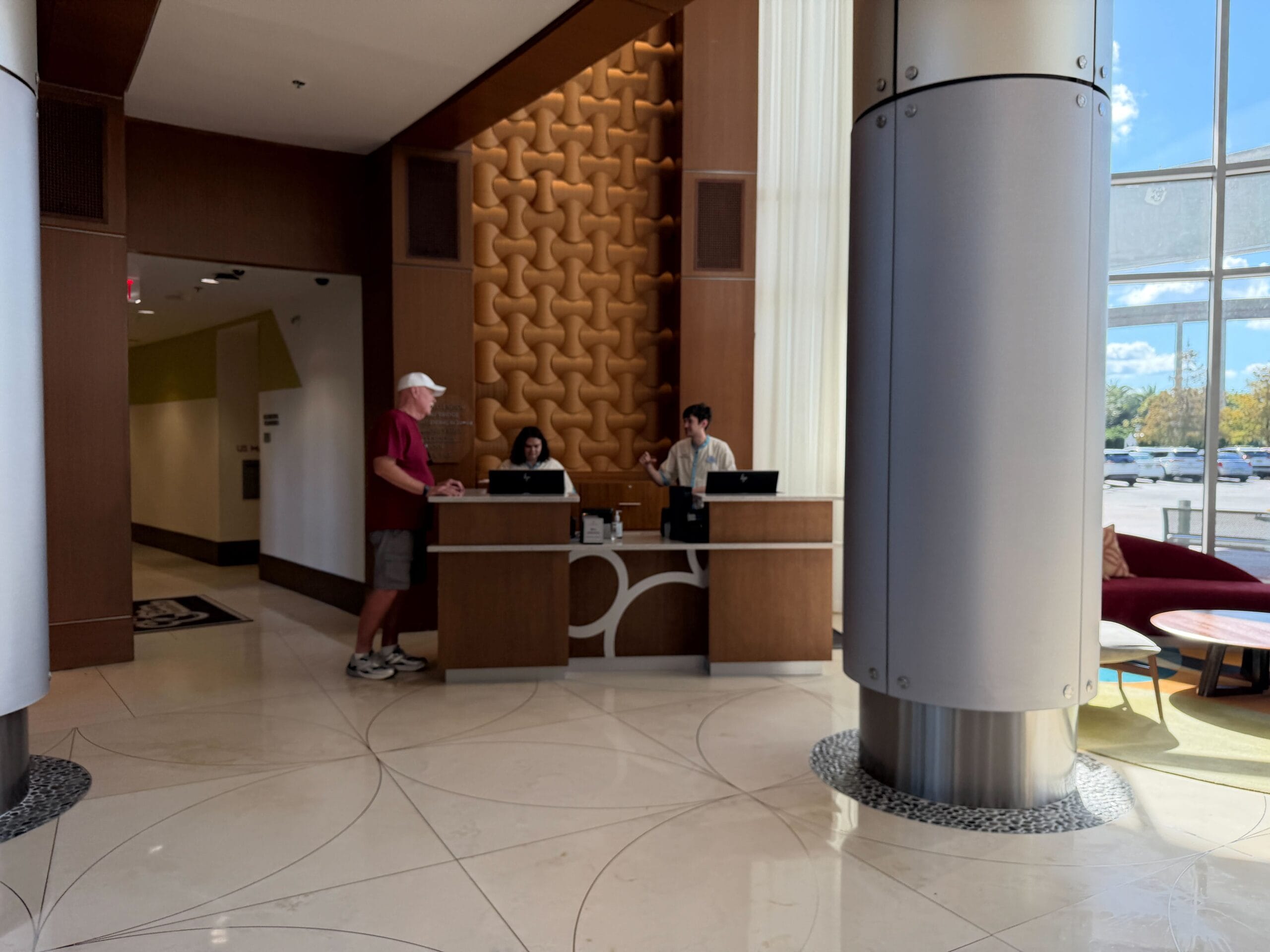 A man chats with two receptionists at the Contemporary Resort front desk, its modern lobby a signature Walt Disney World setting.