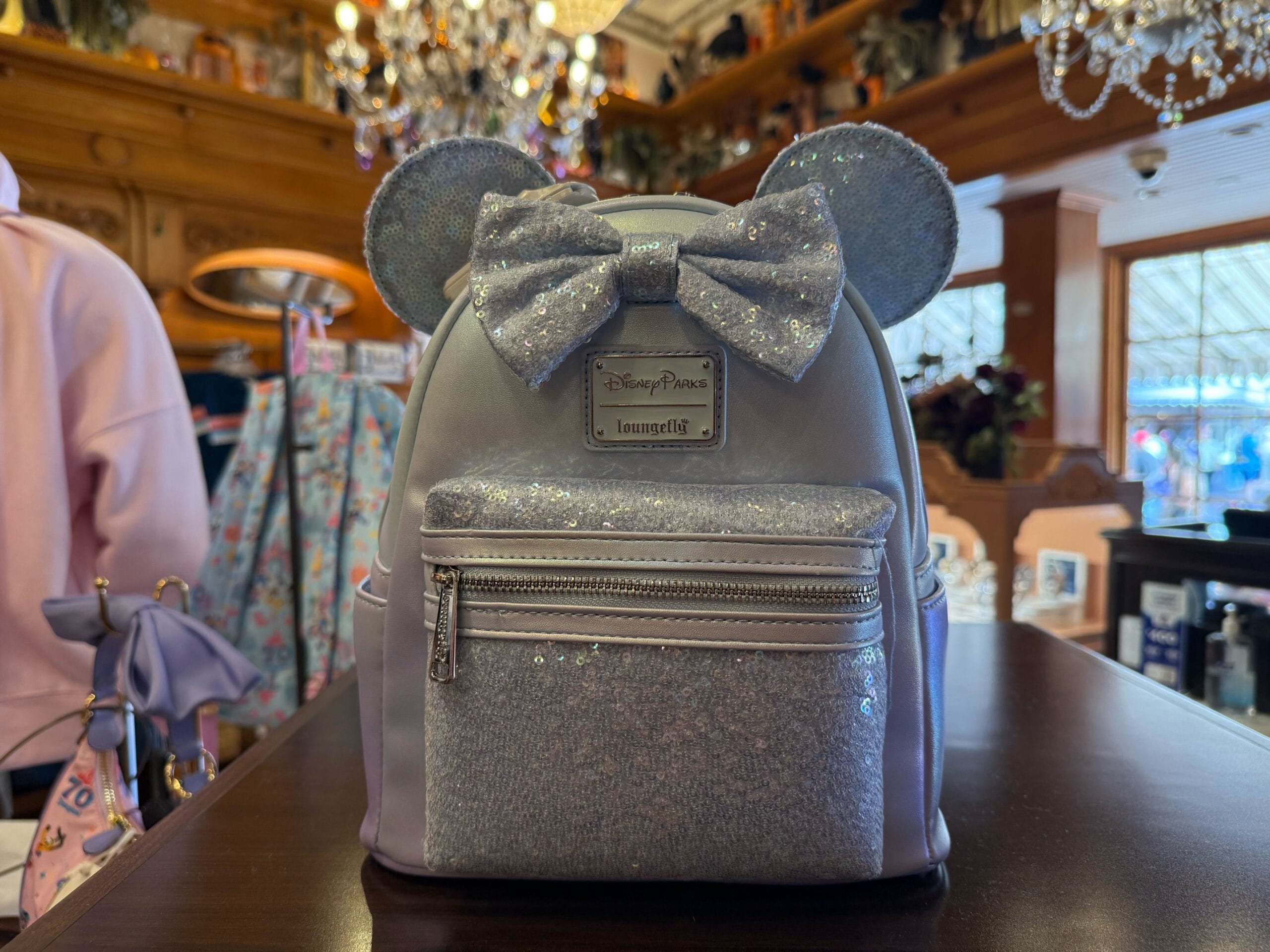 A shimmering silver Disneyland backpack with Minnie ears and a bow shines on display, perfect for park fans at Disney parks worldwide.