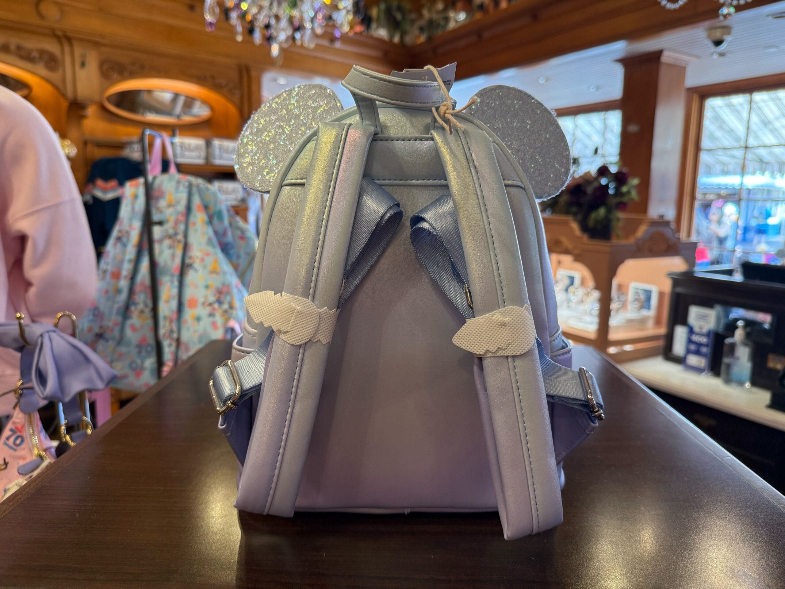 A lavender mini backpack with glittery mouse ears sits next to a Winter Blue Loungefly Backpack, reminiscent of Disney park styles.