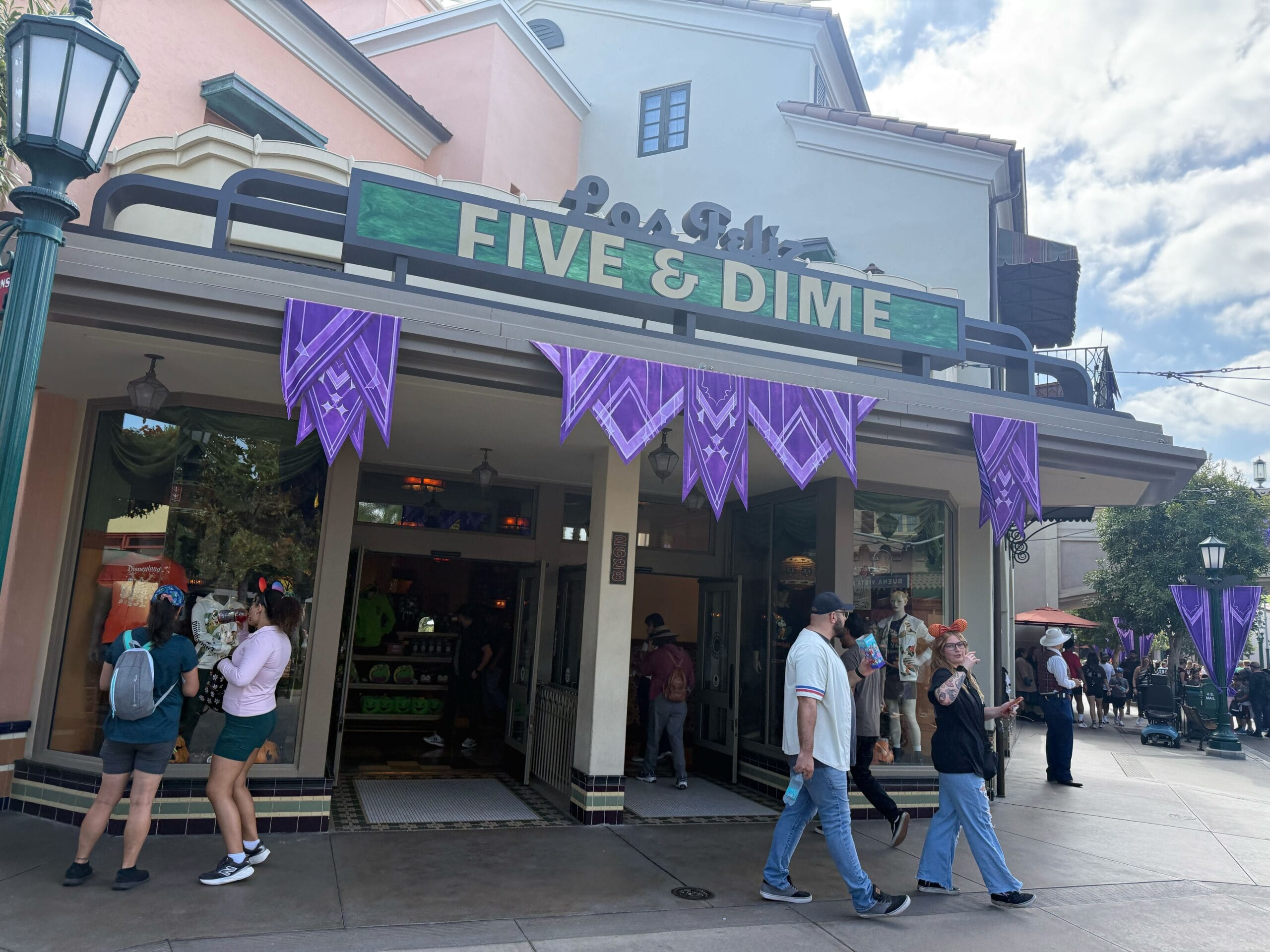 A group of people walking outside a shop at a Disney park, Main Street storefronts visible but no castle in this view.