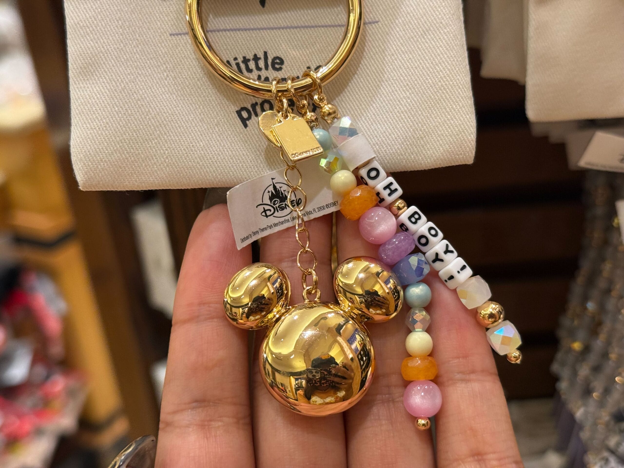 A hand displays a gold Mickey Mouse keychain with vibrant beads spelling “OH BOY!” and a Disney tag, perfect for Disney Parks fans.
