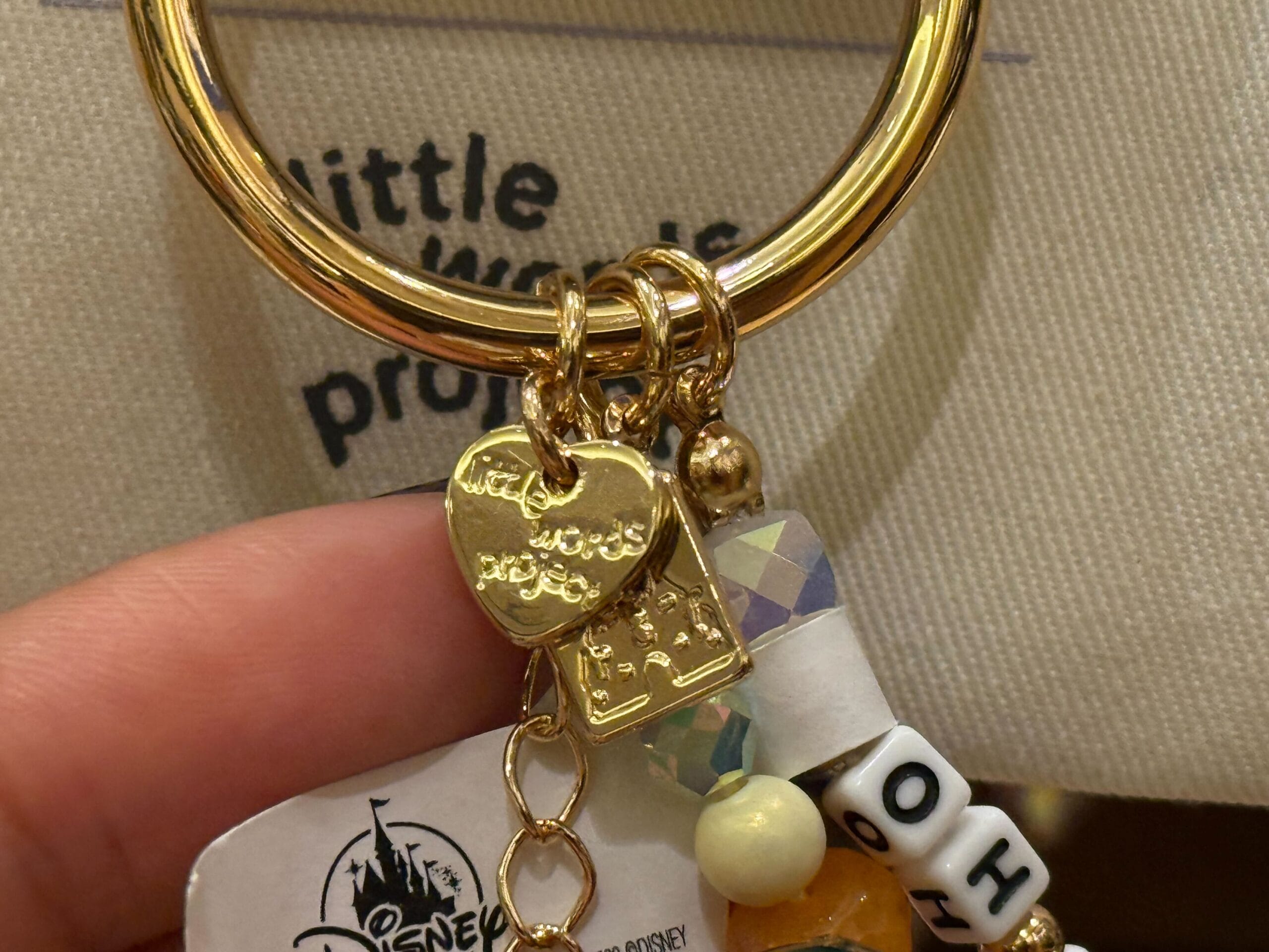 Close-up of a gold keychain with a heart charm, beads, and a small Disney castle charm resembling Cinderella Castle at Disney World.