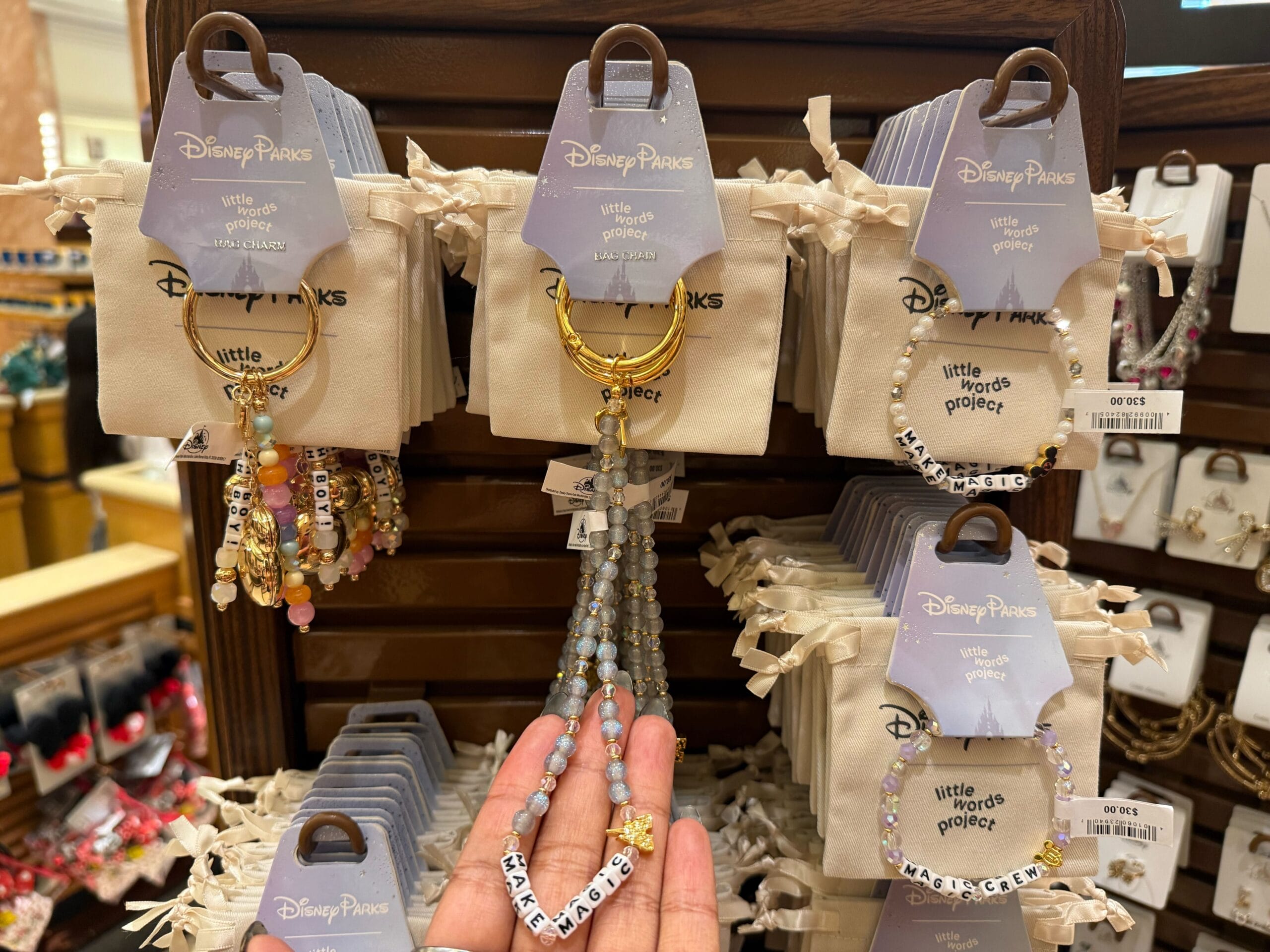 Hand holding a Disney Parks beaded bracelet labeled "Kindness" among other colorful bracelets, displayed at a Disney park gift shop.