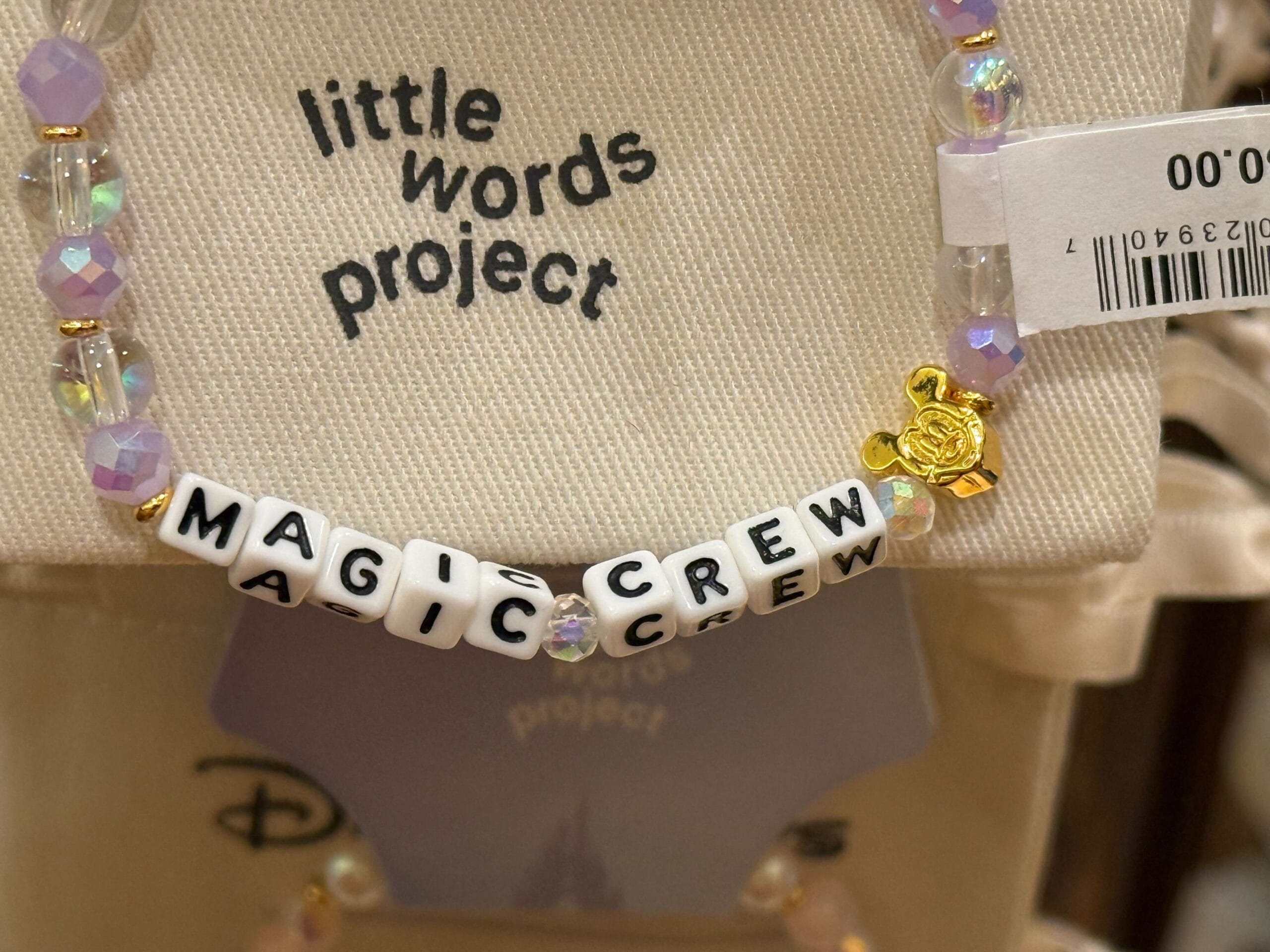 Close-up of a "MAGIC CREW" beaded bracelet featuring a gold Mickey charm, on a "little words project" card, Disney Parks edition.