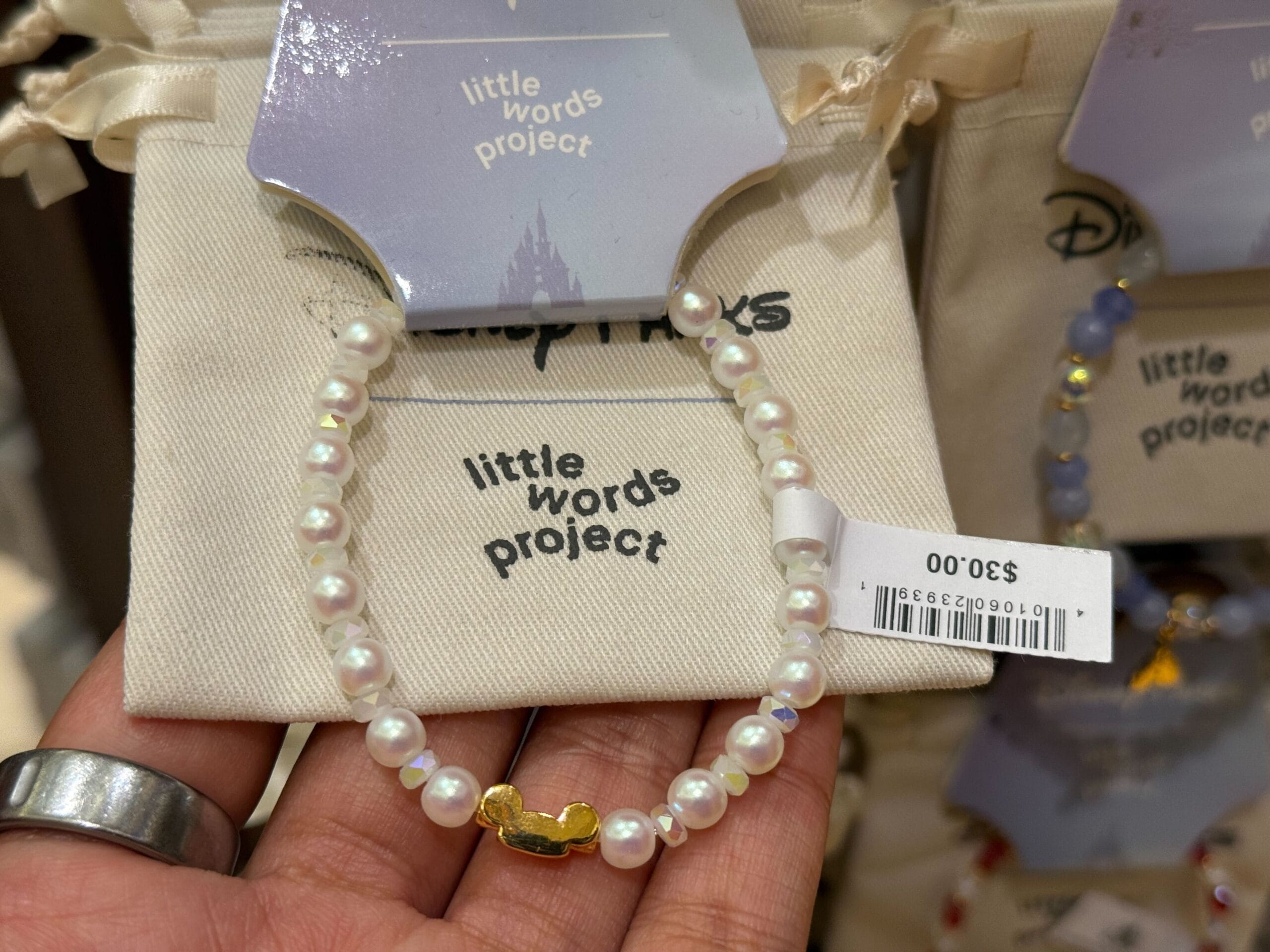 A hand displays a $30 Little Words Project pearl bracelet with a gold Mickey Mouse charm, perfect for Disney Parks fans.