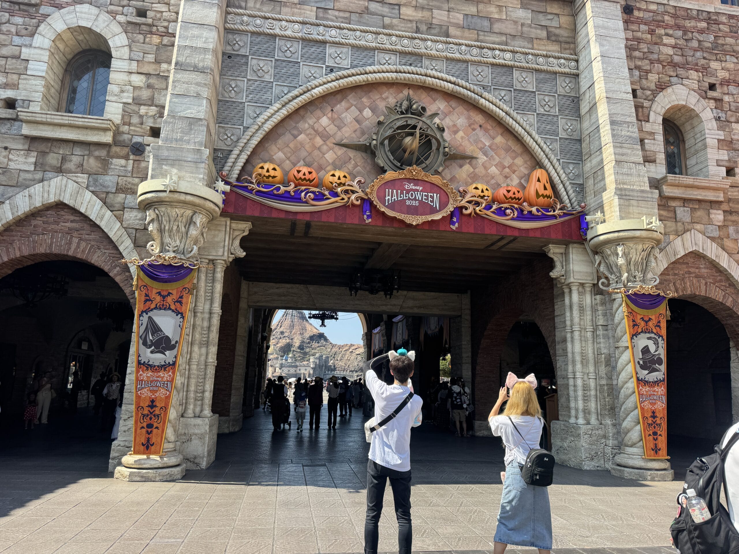 Guests take photos by a pumpkin-filled Halloween arch at Tokyo Disney Resort’s entrance—note there’s no castle like Cinderella Castle here.