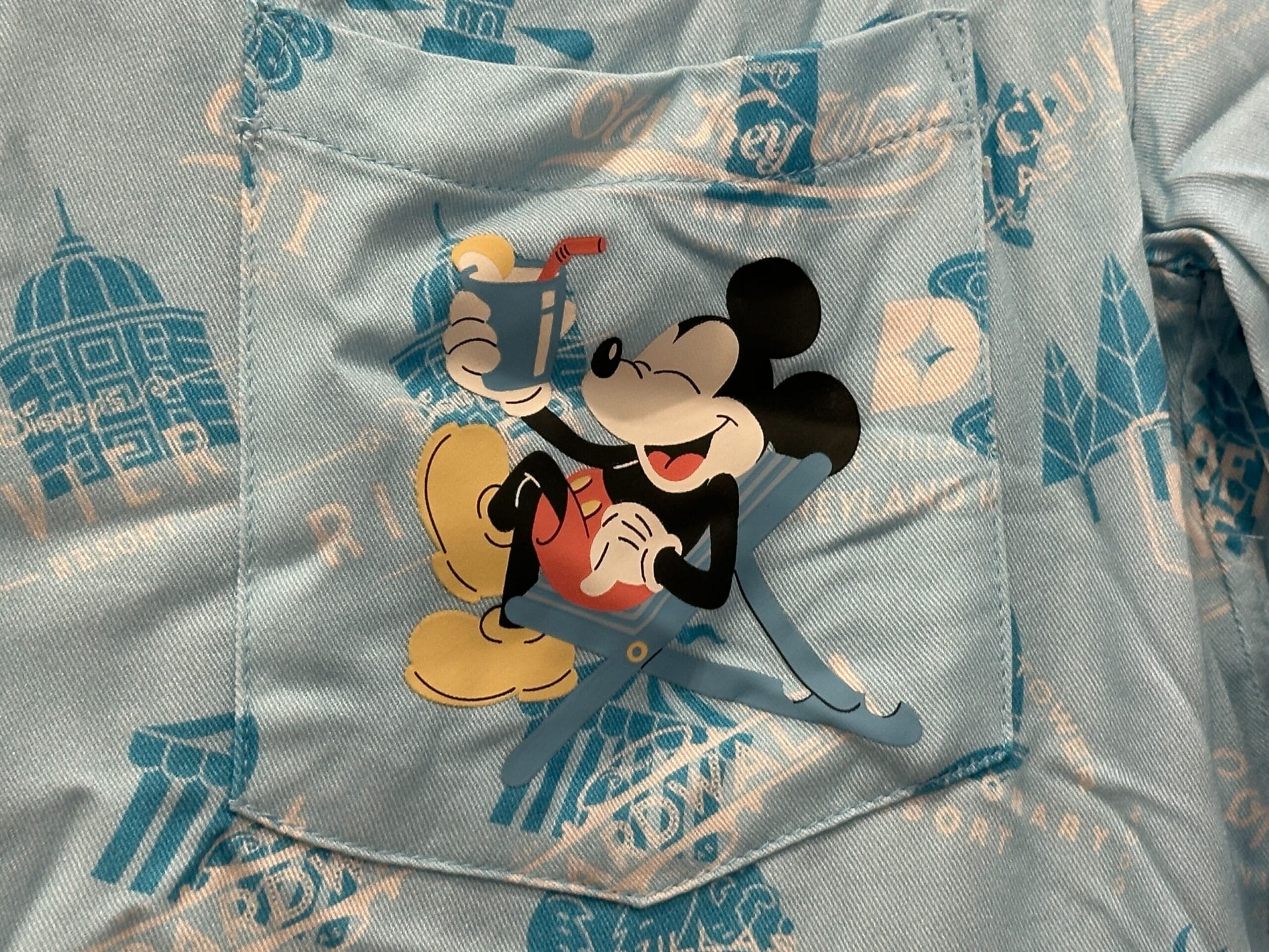 Mickey Mouse relaxes on a blue shirt with vintage Disneyland icons, part of the Grand Floridian Merch Collection.