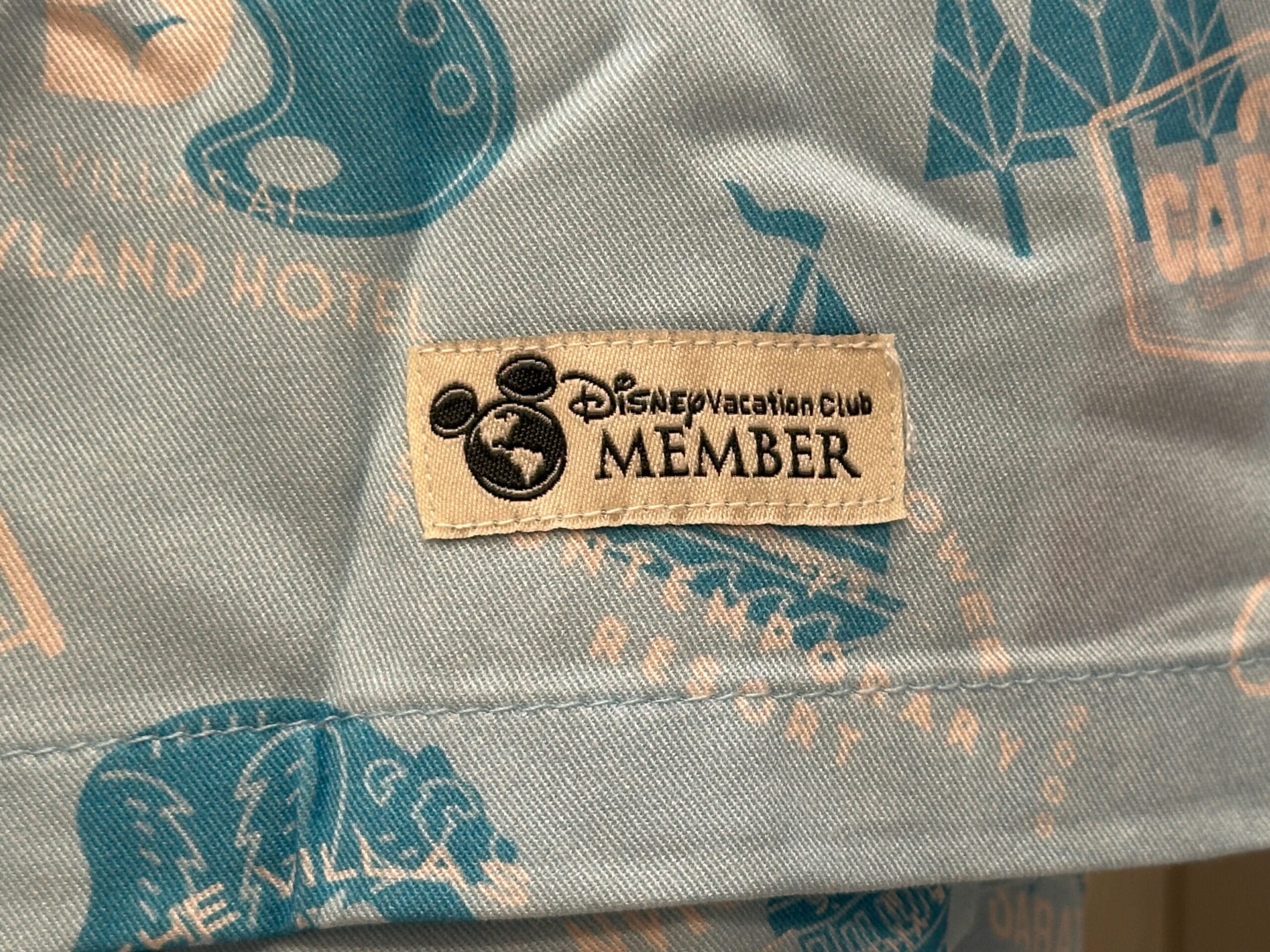 A fabric label from the Merch Collection reads "Disney Vacation Club MEMBER" with a Mickey icon on a blue background.