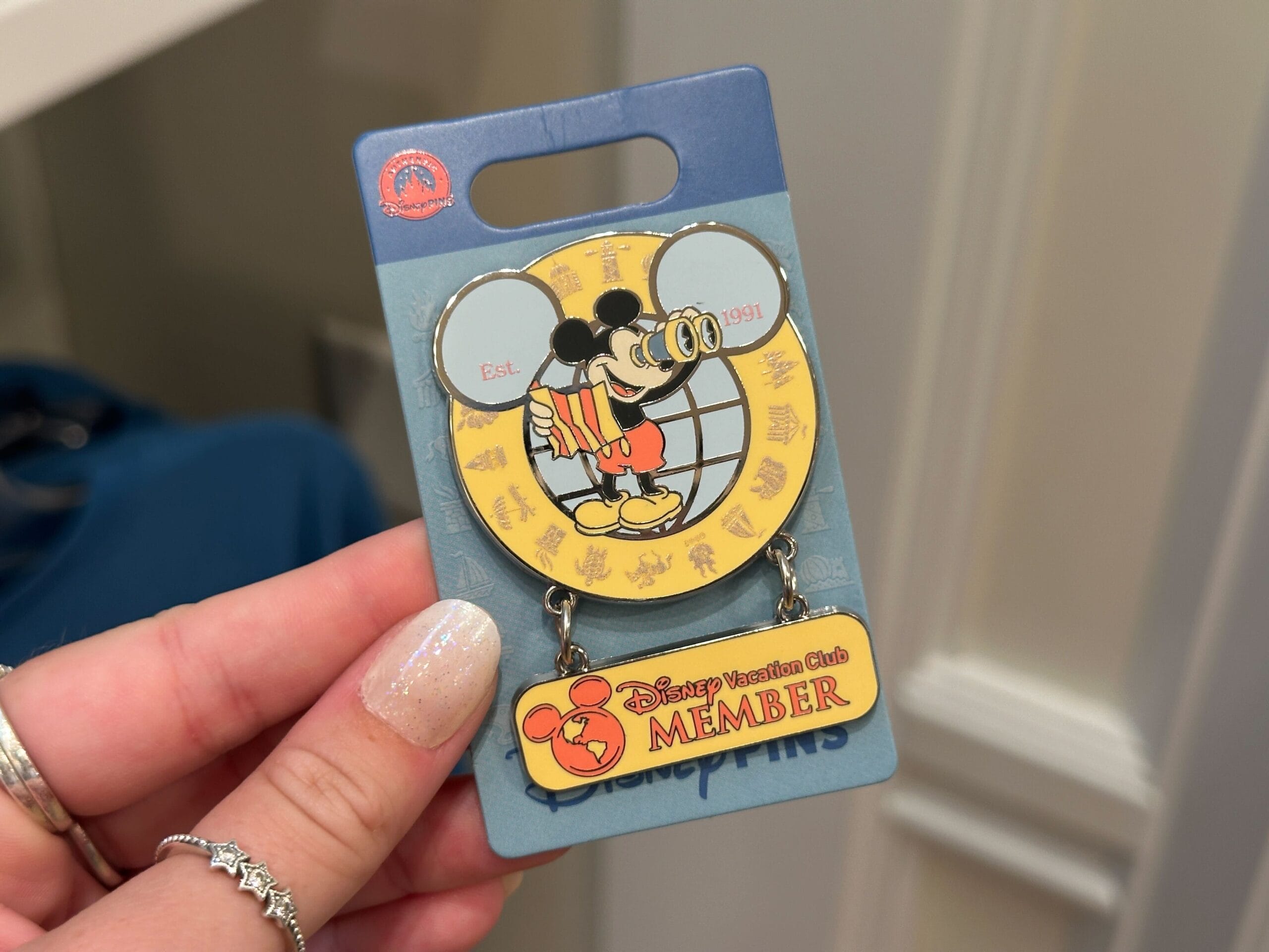 Hand holding a DVC Member pin from the Merch Collection, featuring Mickey Mouse and “Est. 1991” text.