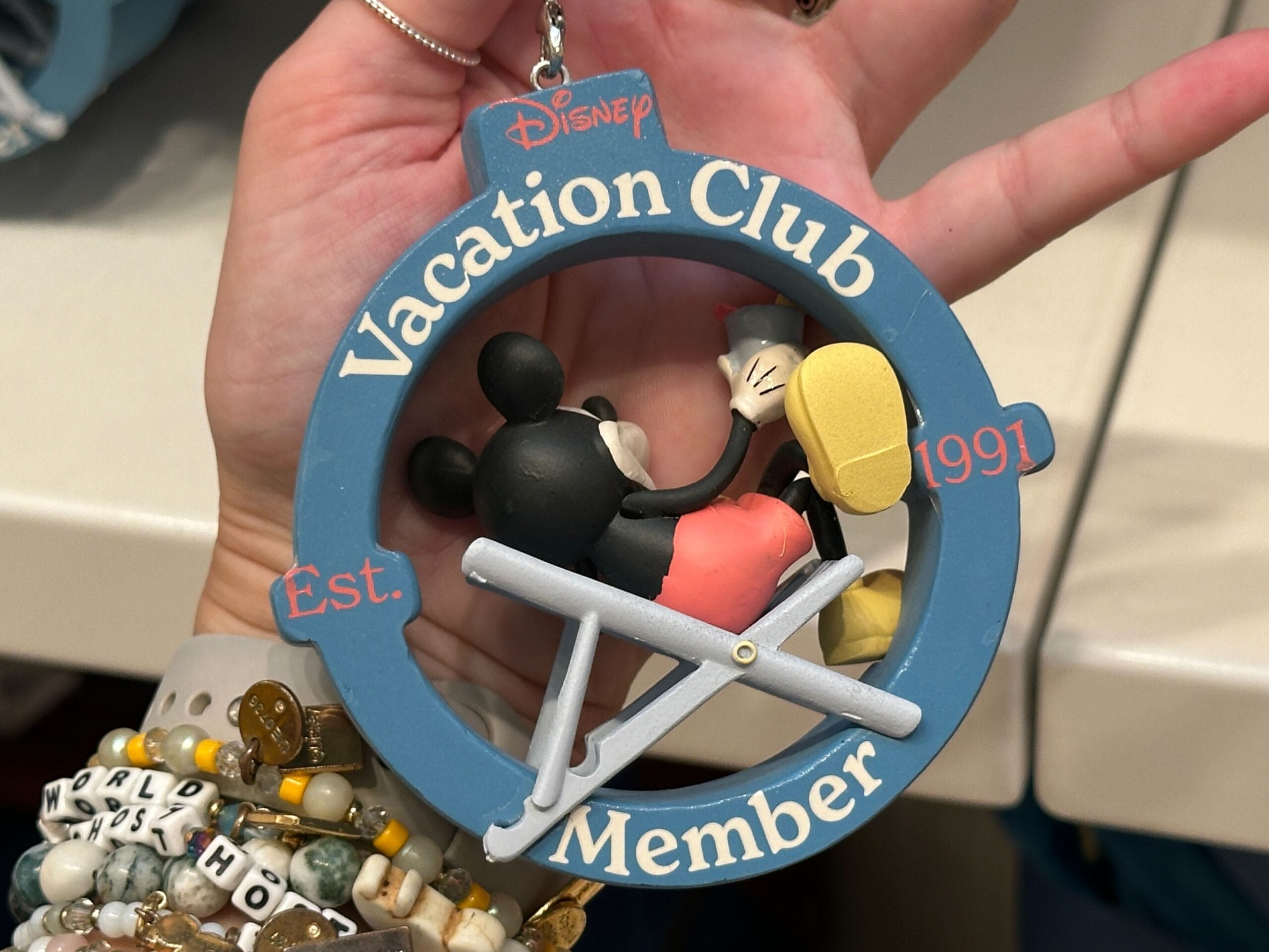 A hand holds a DVC Member Merch ornament with Mickey Mouse lounging in a chair at Grand Floridian.