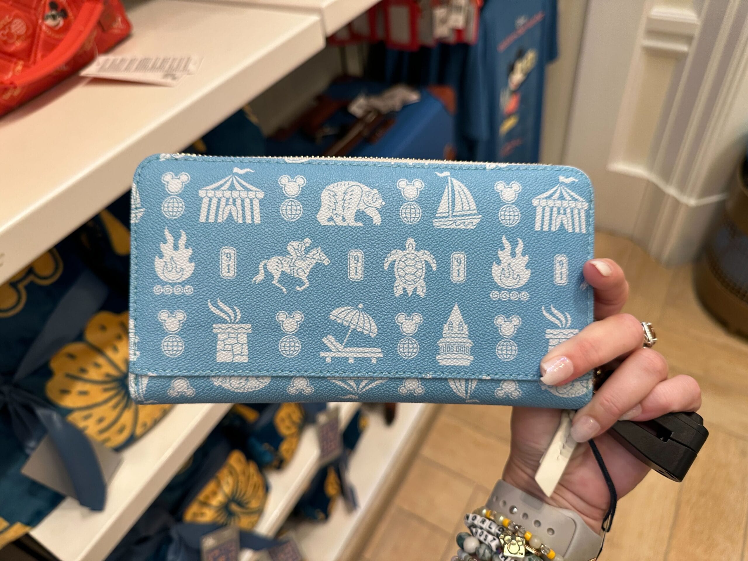 A hand holds a blue wallet from the New Collection, featuring white icons and Disney DVC Member Merch symbols.