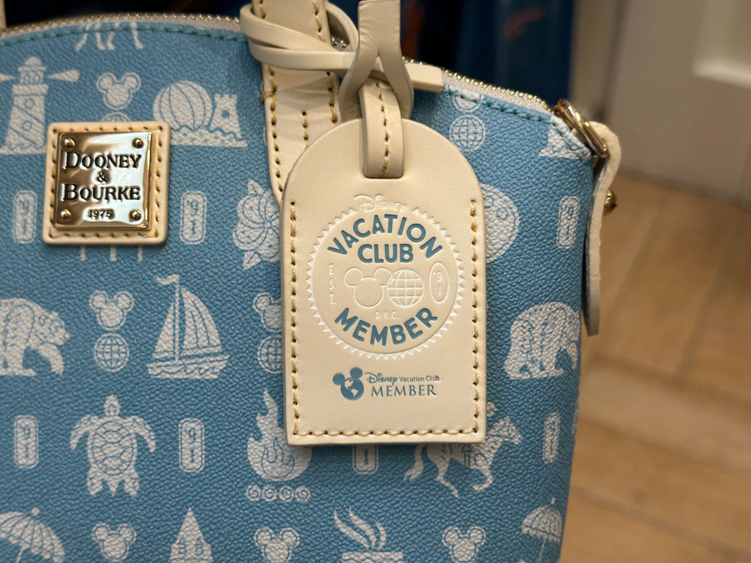 Close-up of a blue Dooney & Bourke bag from the DVC Member Merch New Collection with a Disney Vacation Club tag.