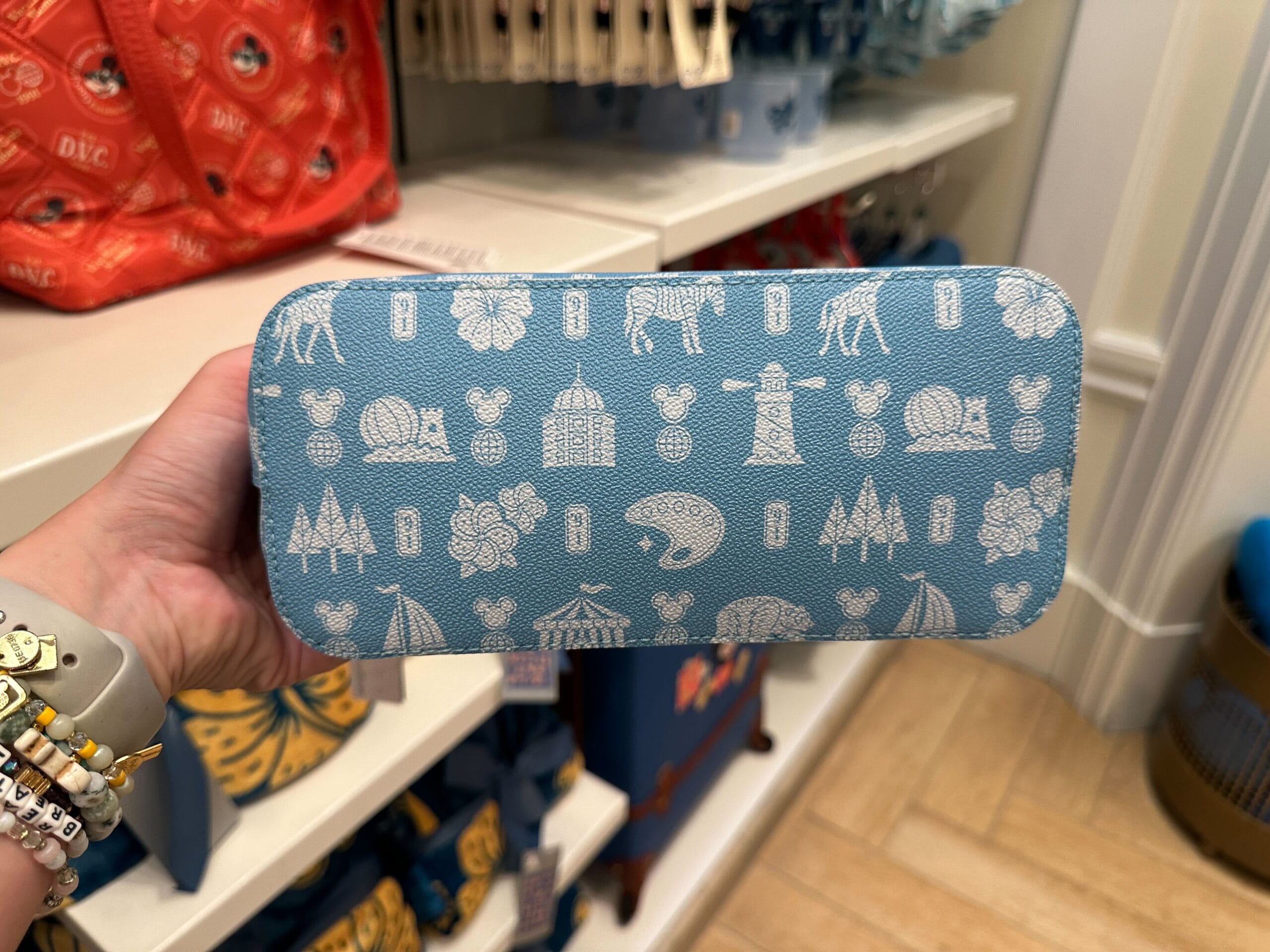 A hand holds a blue case with white animal and castle patterns from the new Grand Floridian collection in a themed store.