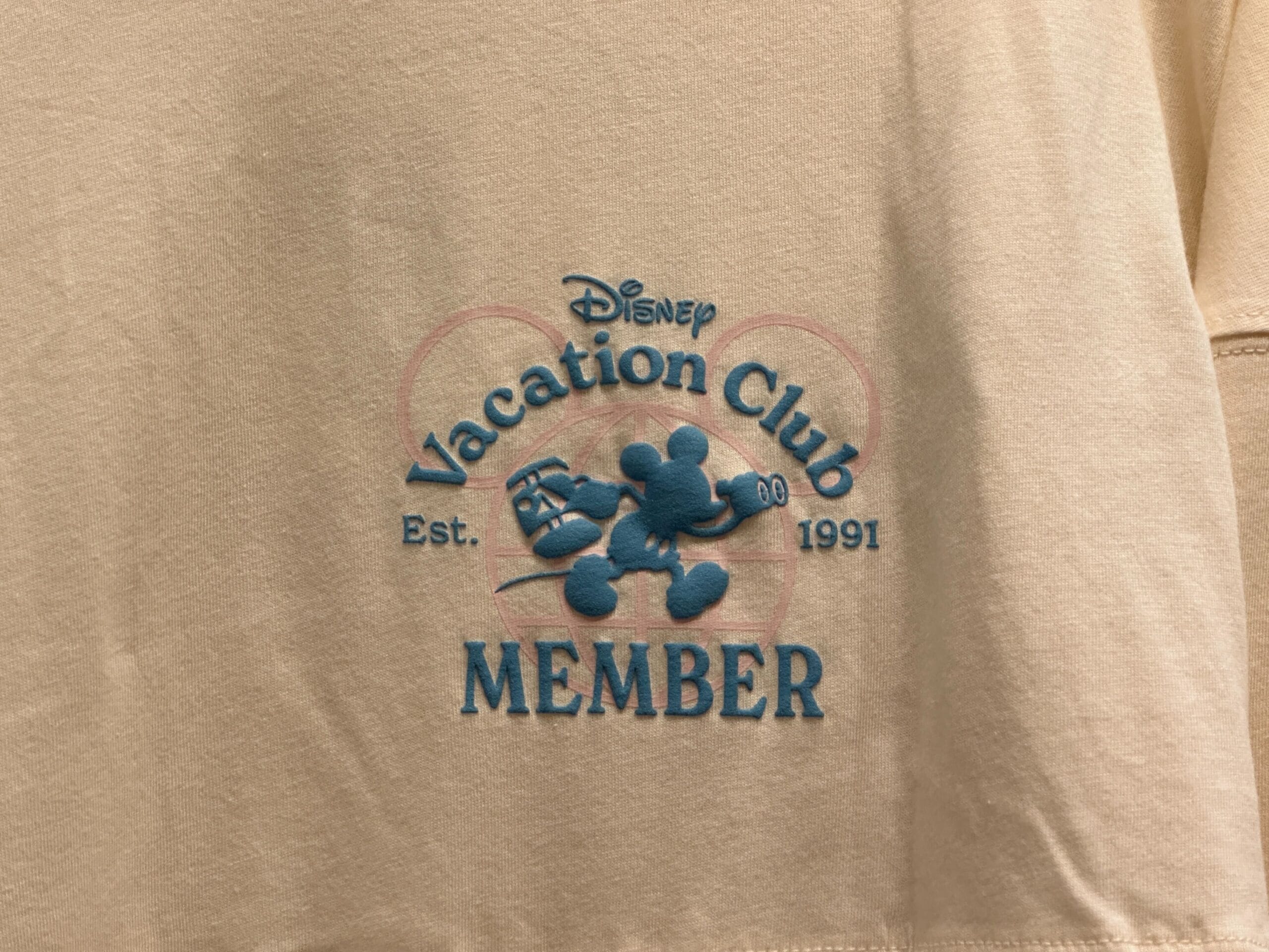 Close up of cream Disney Vacation Club Member-exclusive Spirit Jersey with a blue Mickey Mouse on the chest and the text "Disney Vacation Club Member Est. 1991."
