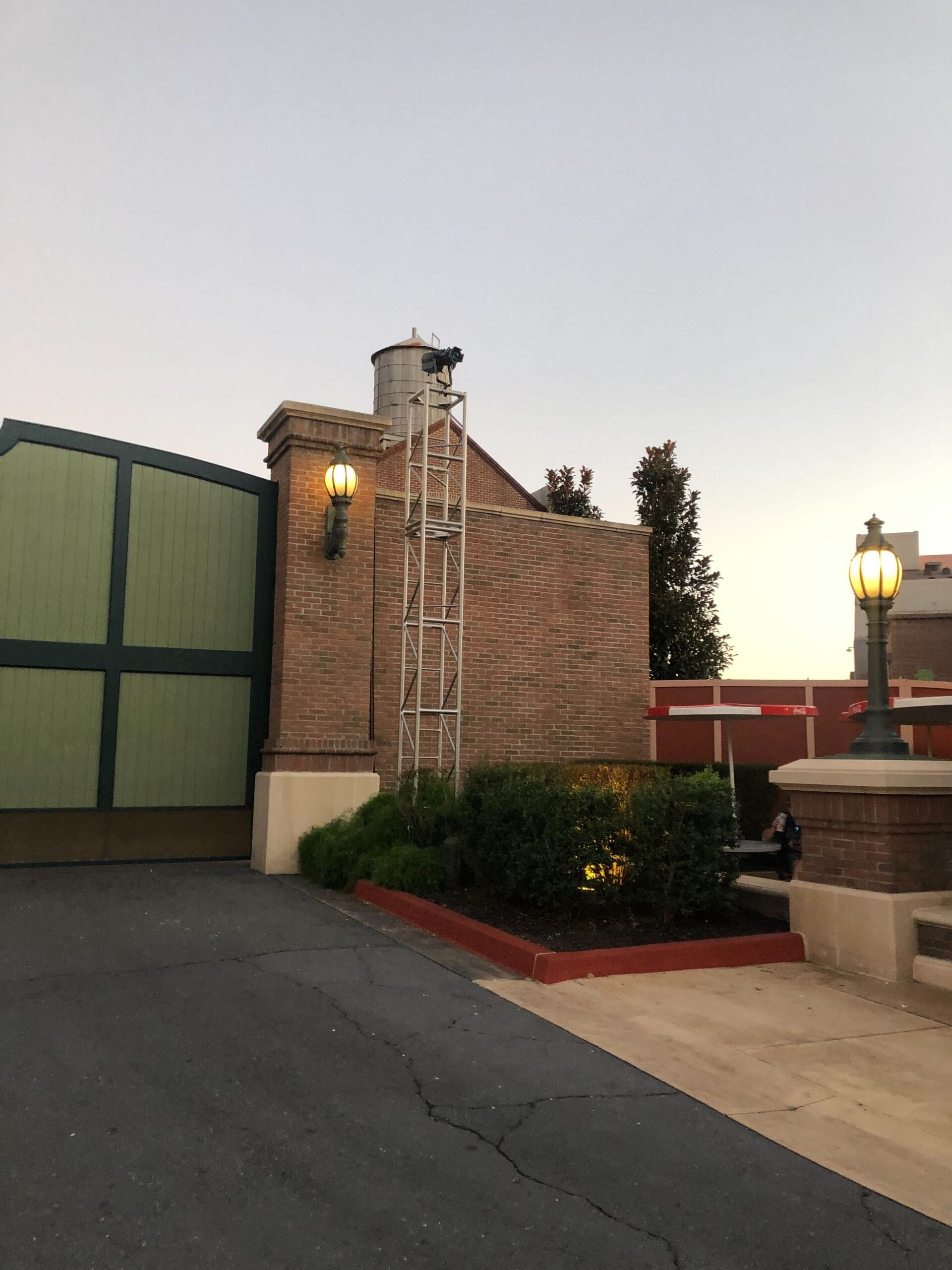 A brick building with green doors and vintage lamps at dusk, reminiscent of Hollywood Studios’ classic Disney atmosphere.