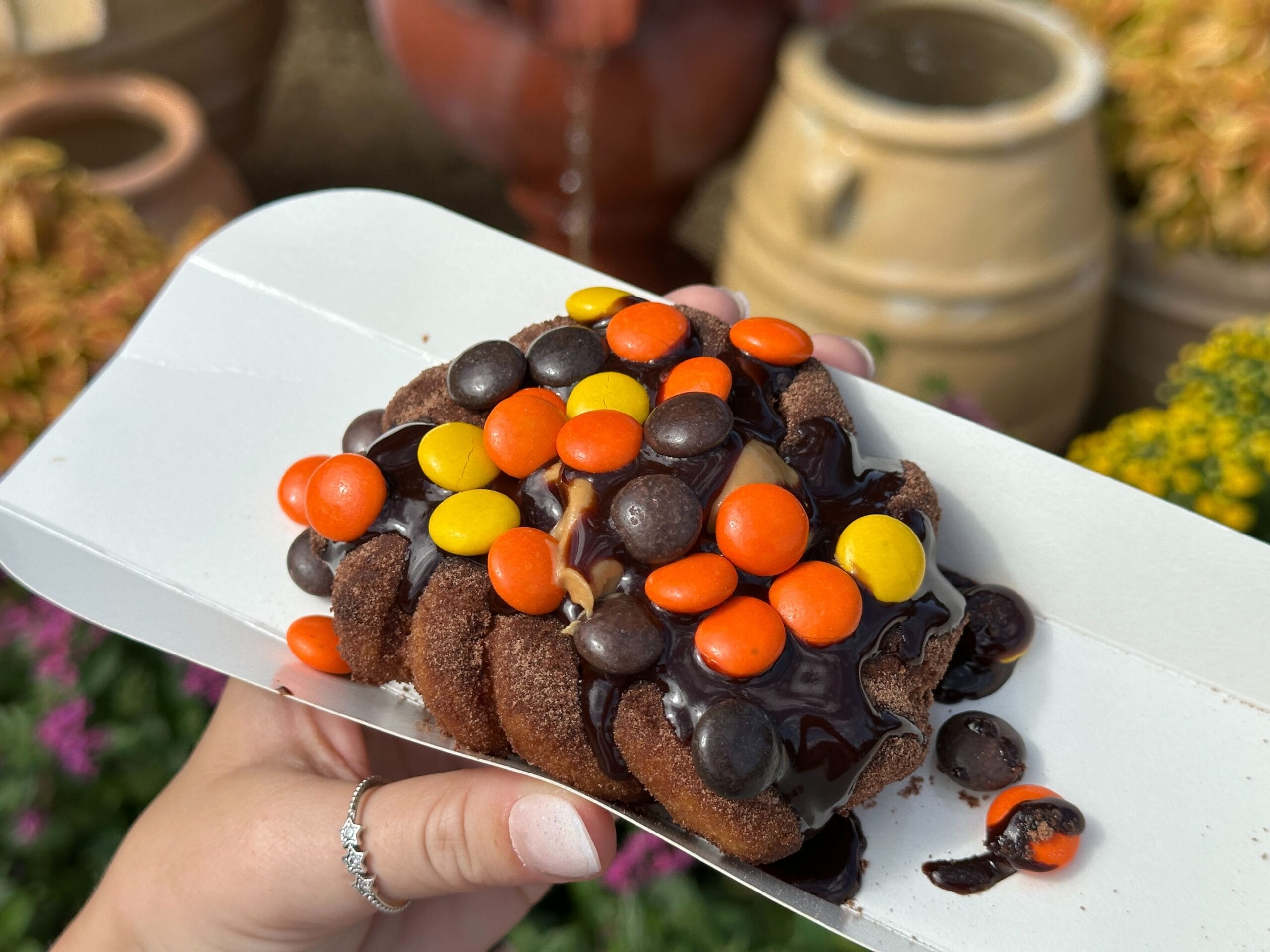 A chocolate dessert topped with brightly colored candy-coated chocolates and chocolate sauce on a paper tray.