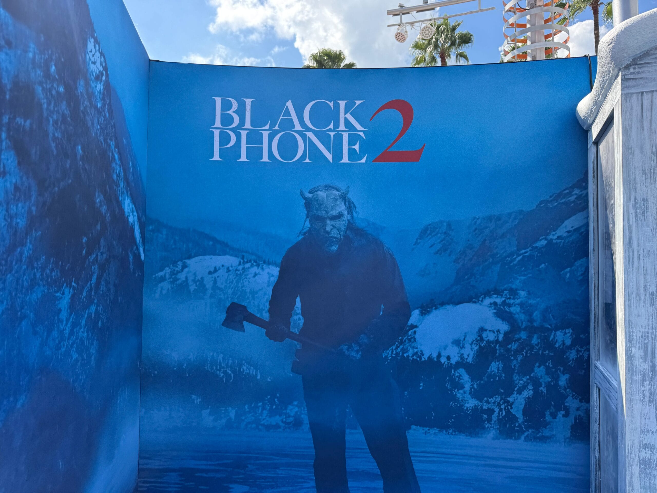 A "Black Phone 2" poster by Blumhouse features a masked figure with an axe in a snowy, mountainous landscape.