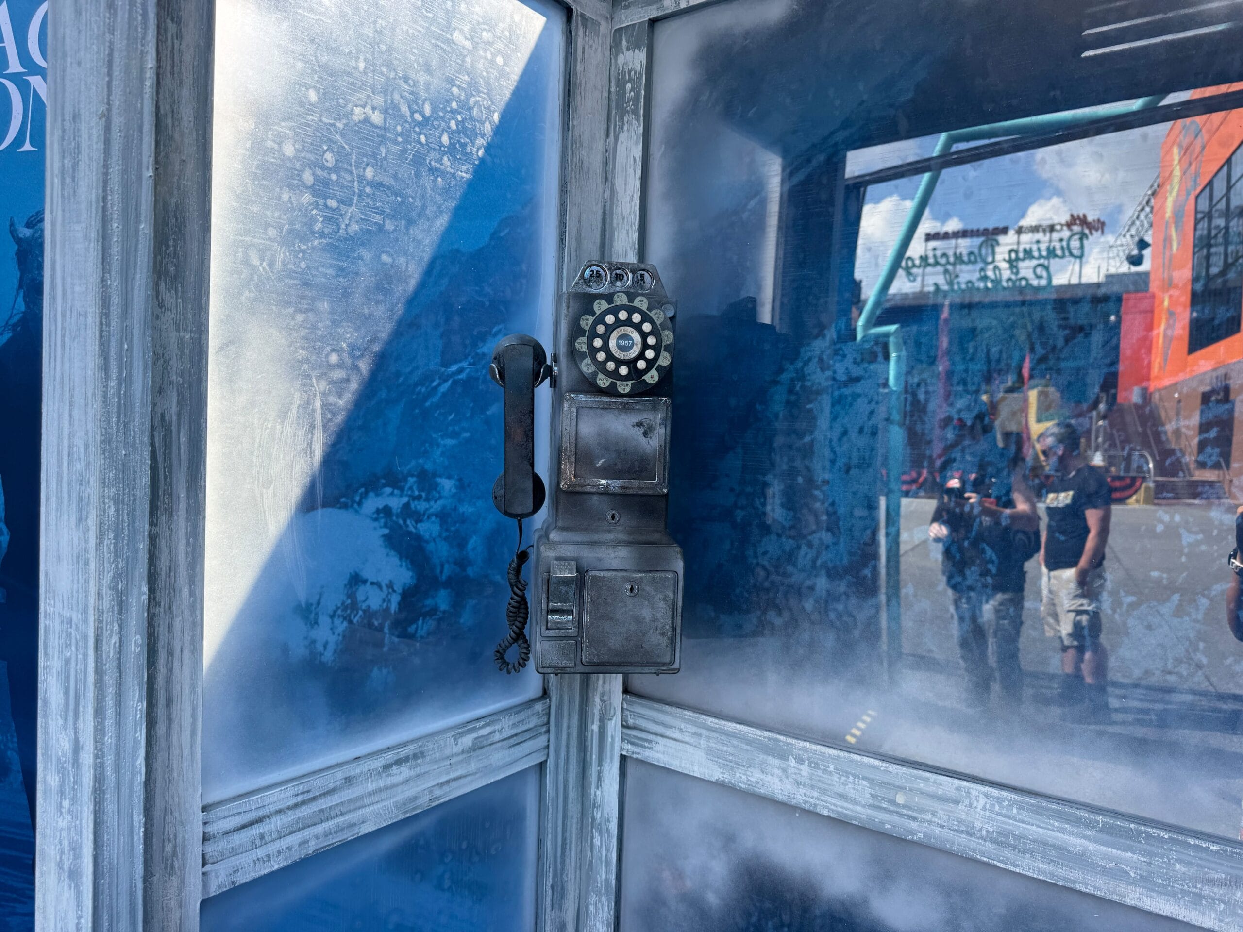 A vintage rotary payphone sits in a frosted glass booth at Universal CityWalk, people reflected outside.