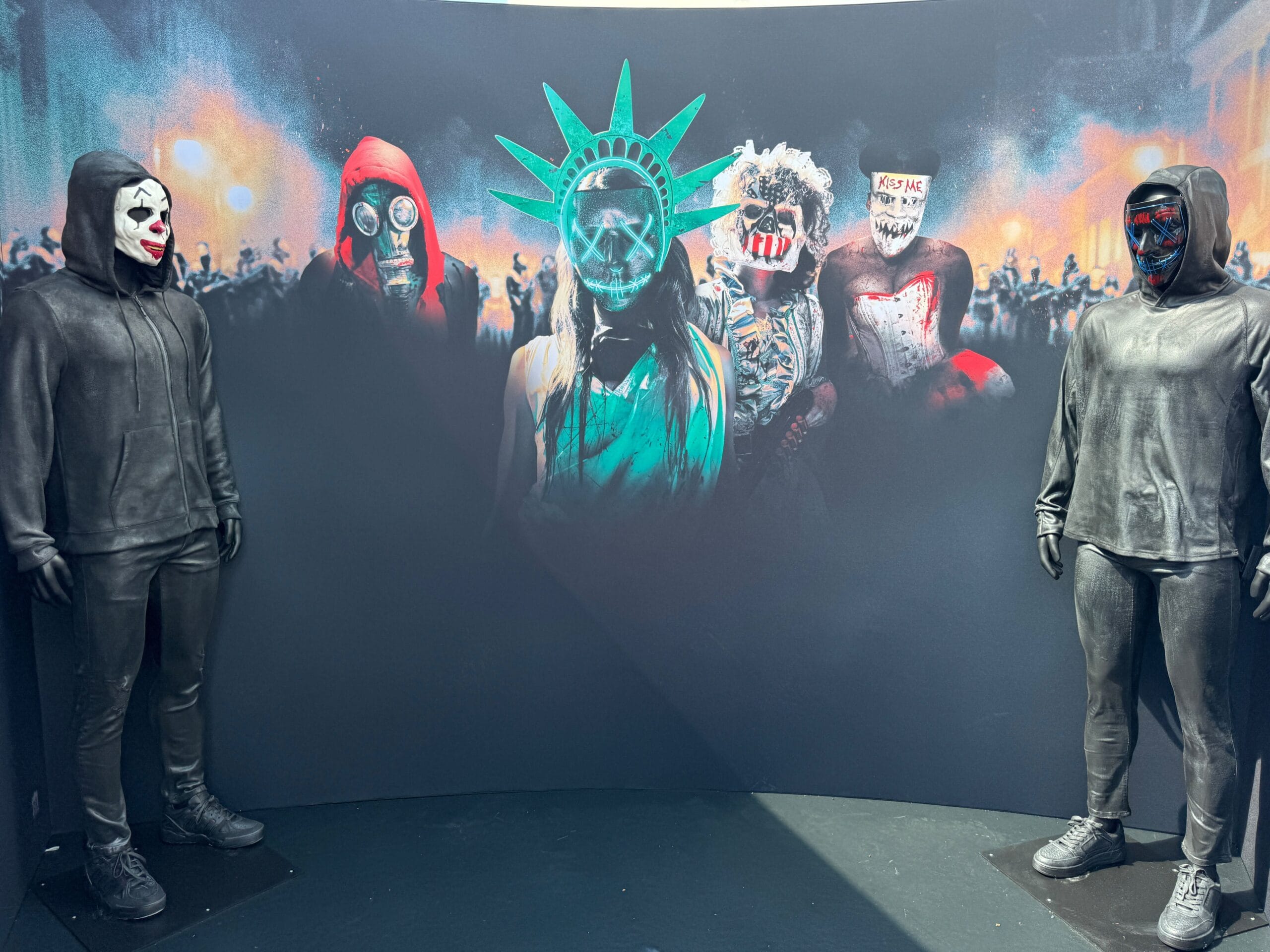 Two mannequins in black hoodies flank a mural at Universal CityWalk featuring masked figures and a graffiti-style Liberty mask.